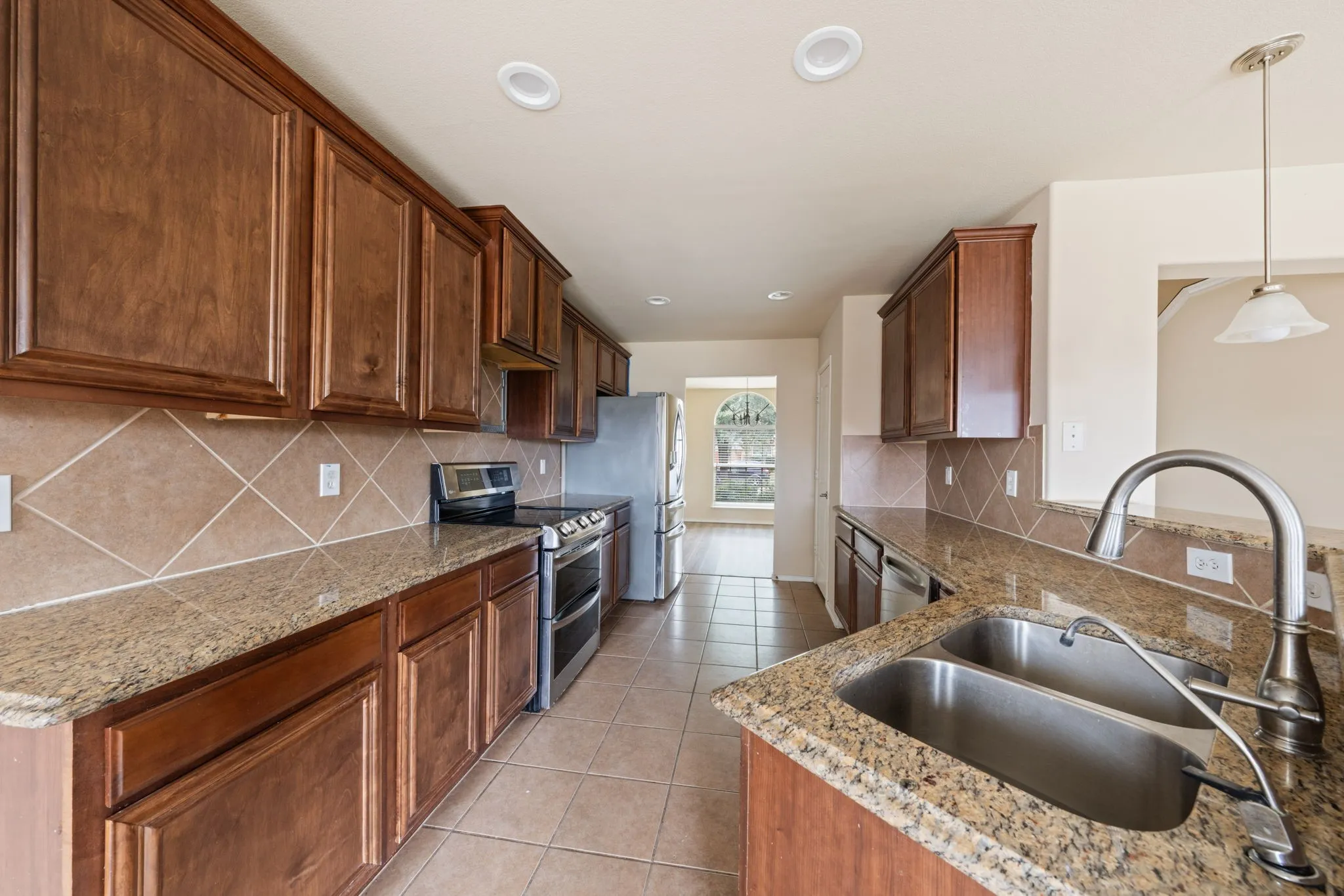 Kitchen featuring appliances with stainless steel finishes, decorative backsplash, light tile patterned floors, pendant lighting, and light stone countertops