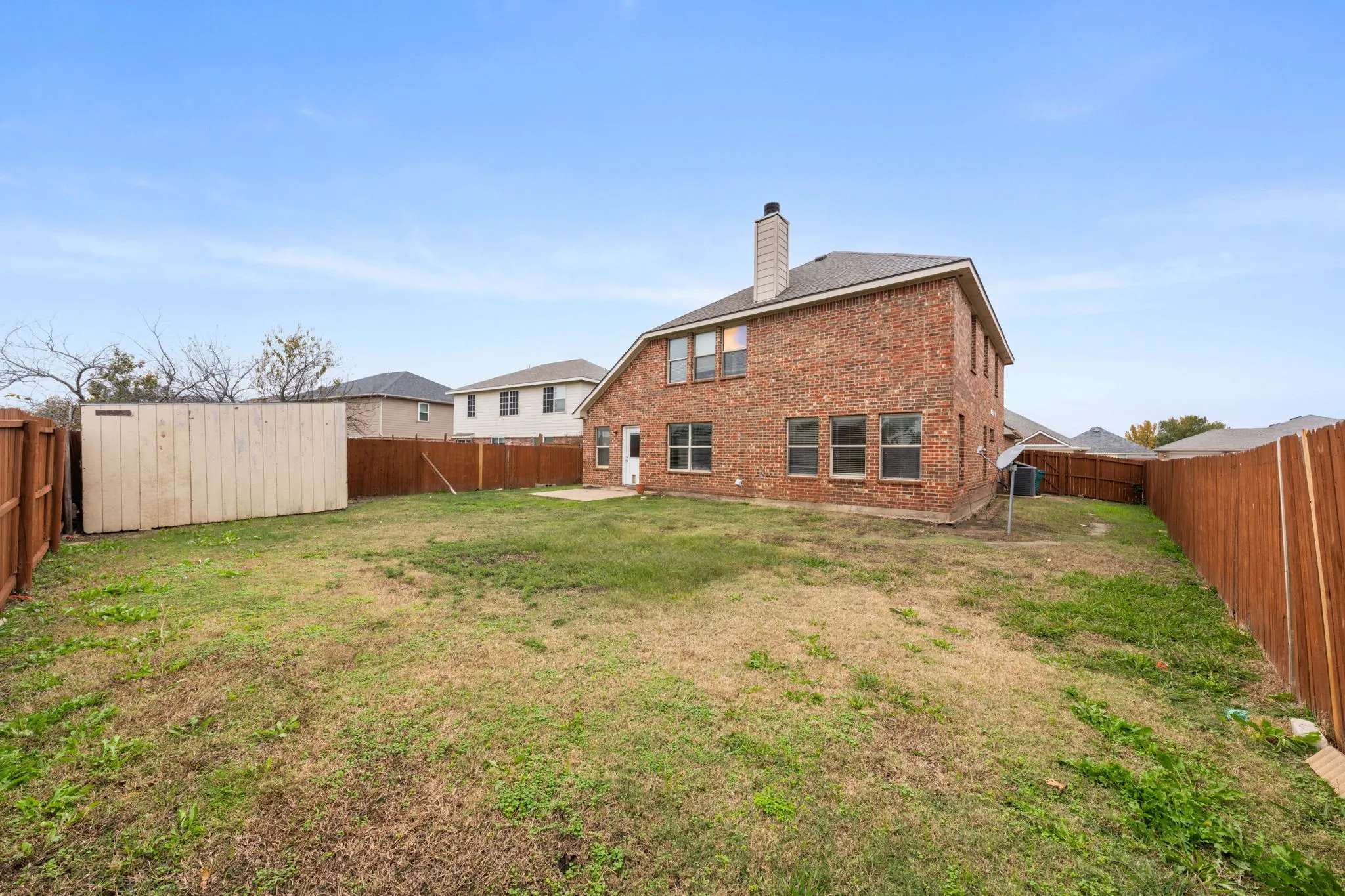 Rear view of house featuring a chimney, a patio area, a fenced backyard, and brick siding