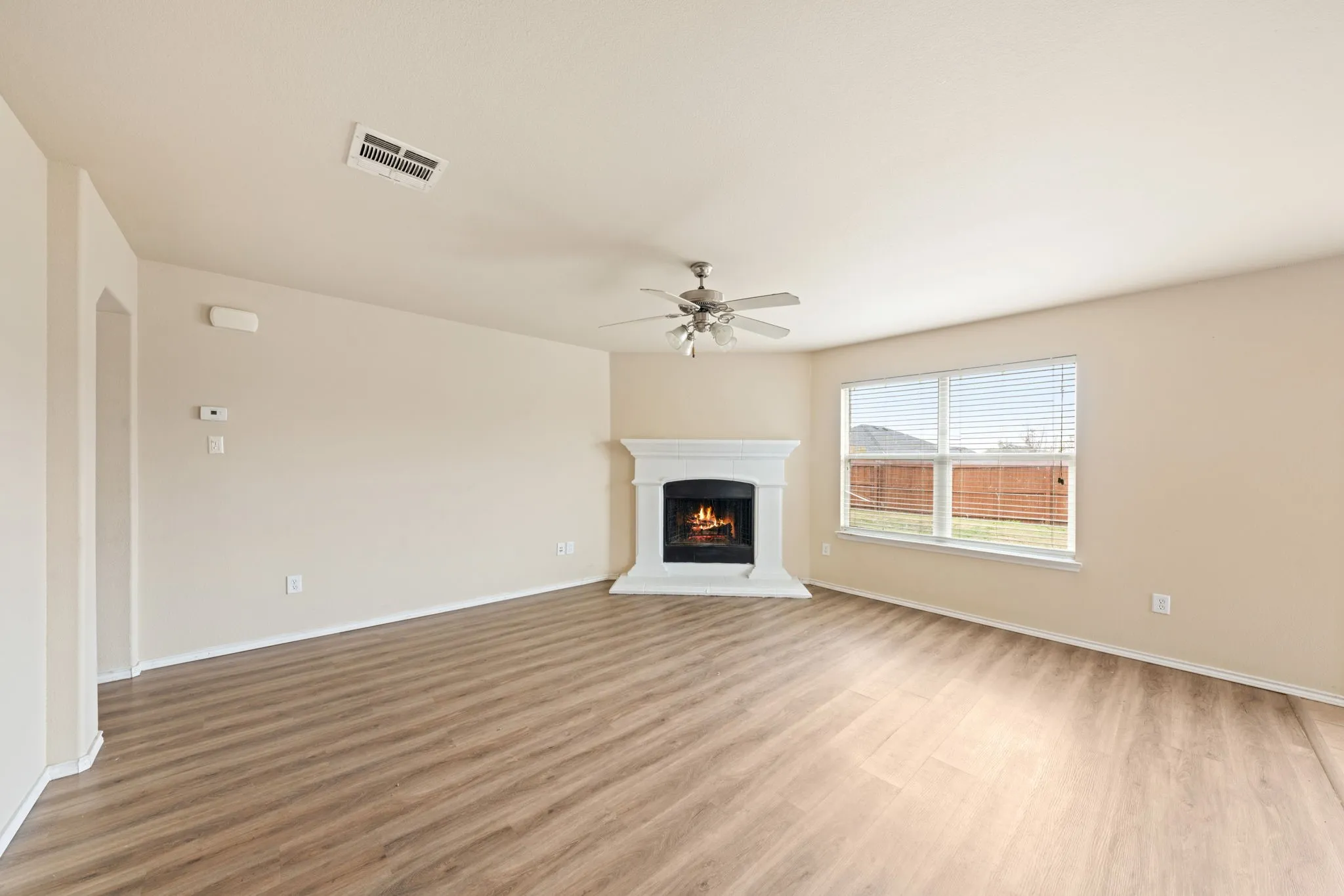 Unfurnished living room featuring a lit fireplace, light wood-type flooring, and a ceiling fan