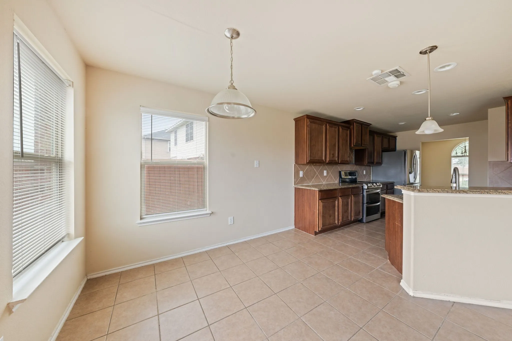 Kitchen with tasteful backsplash, pendant lighting, range with two ovens, light stone countertops, and light tile patterned floors