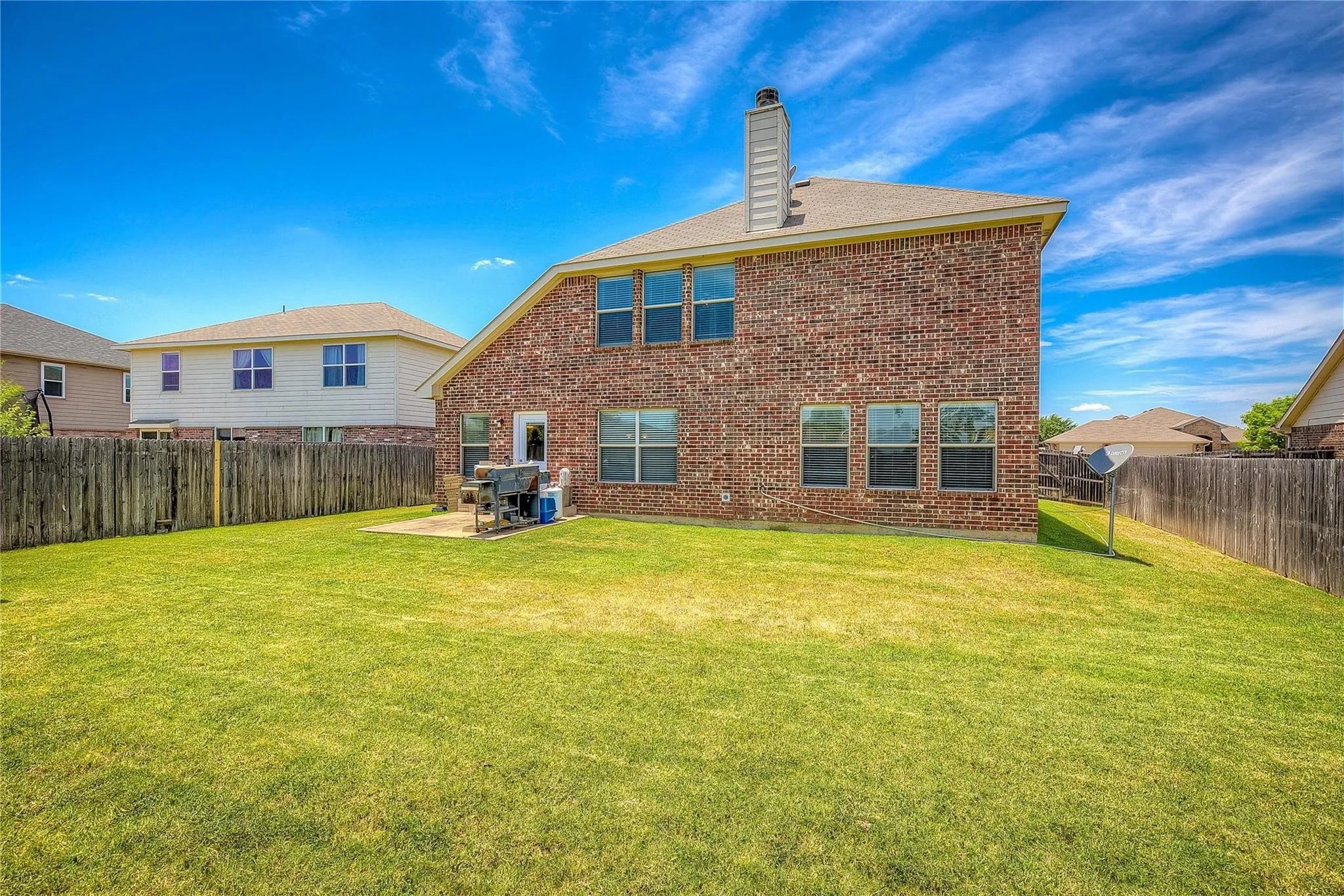 Rear view of house with brick siding, a chimney, a fenced backyard, and a patio area