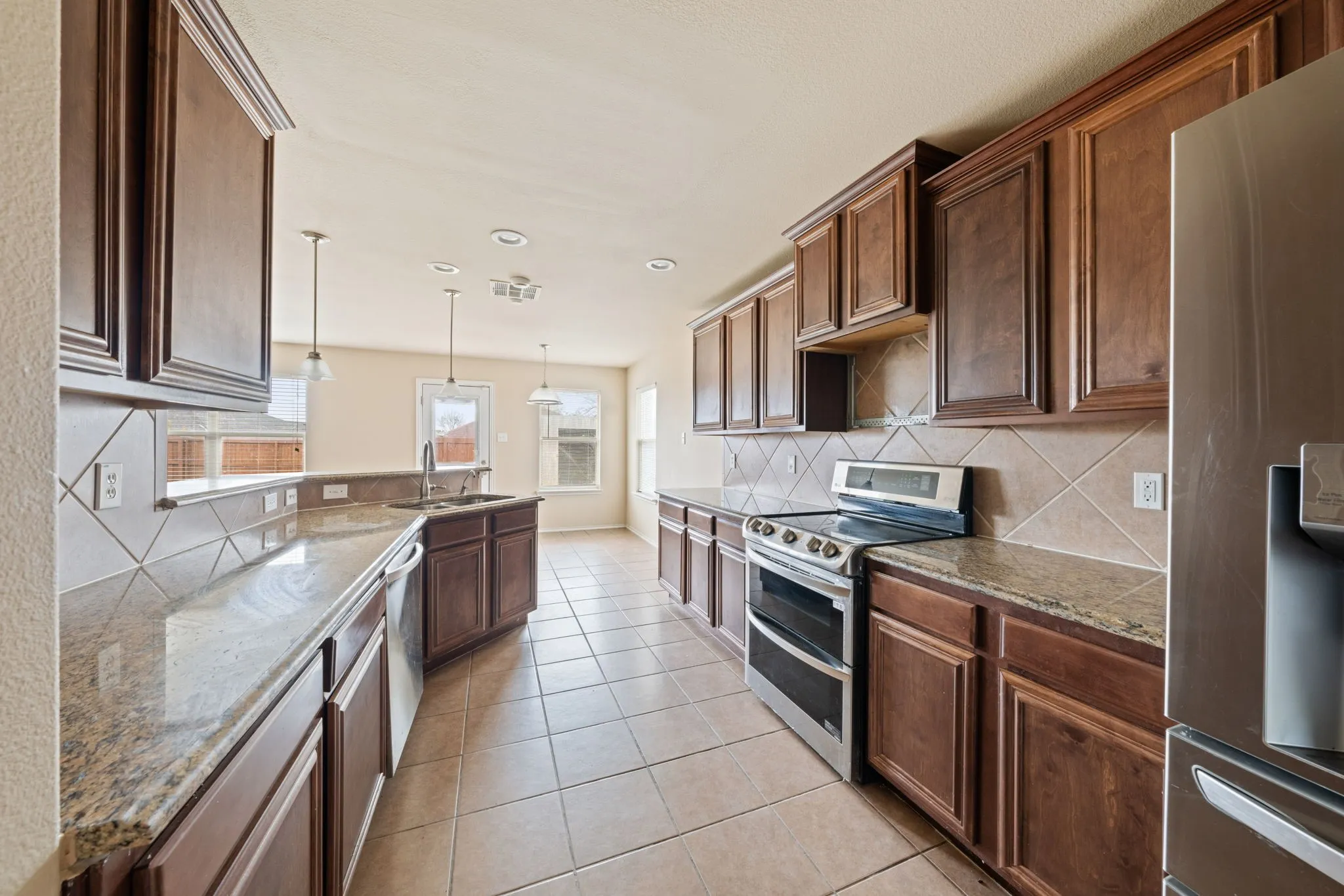 Kitchen featuring appliances with stainless steel finishes, pendant lighting, light stone countertops, recessed lighting, and light tile patterned flooring