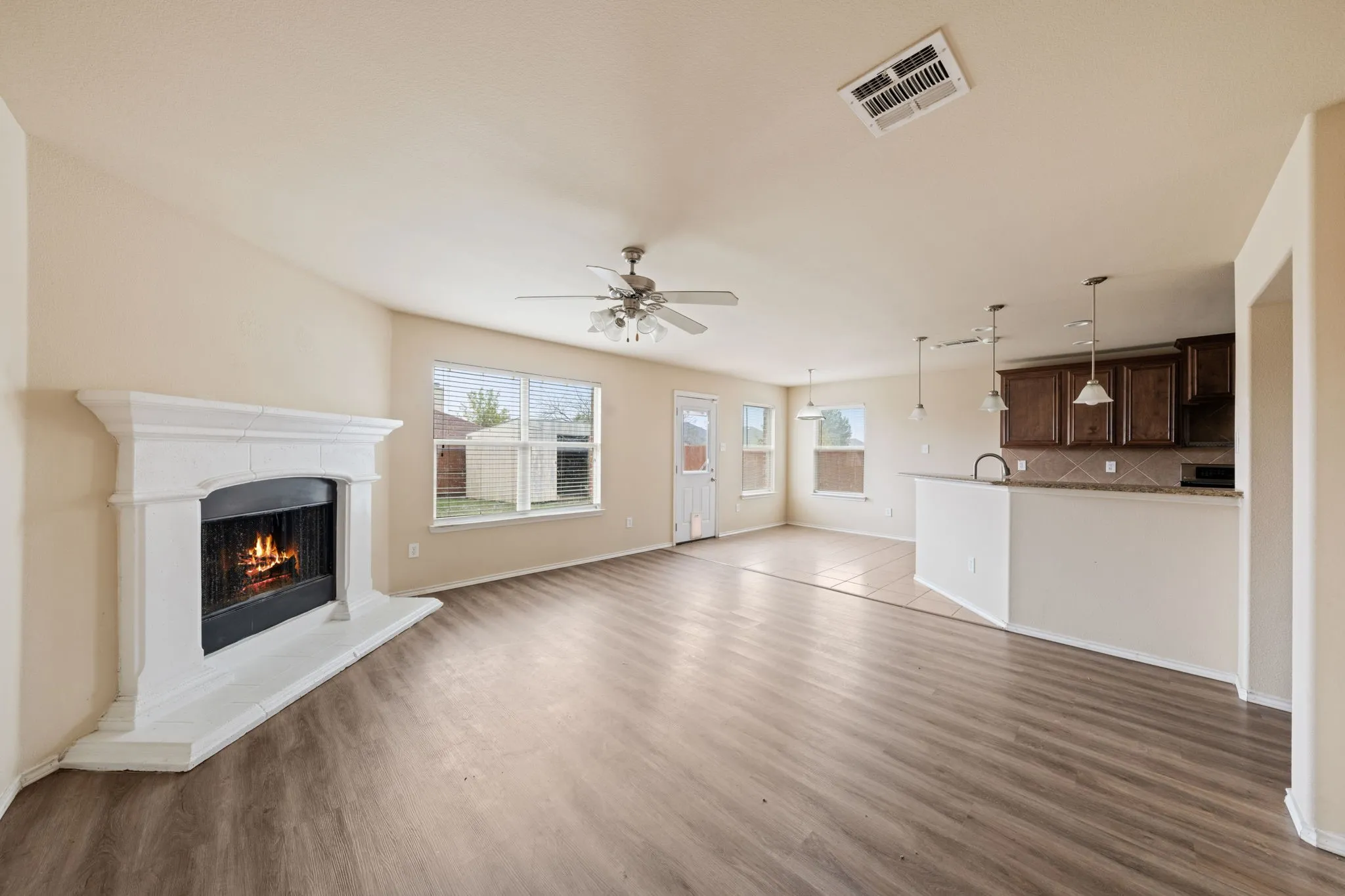 Unfurnished living room with a warm lit fireplace, light wood-type flooring, and a ceiling fan