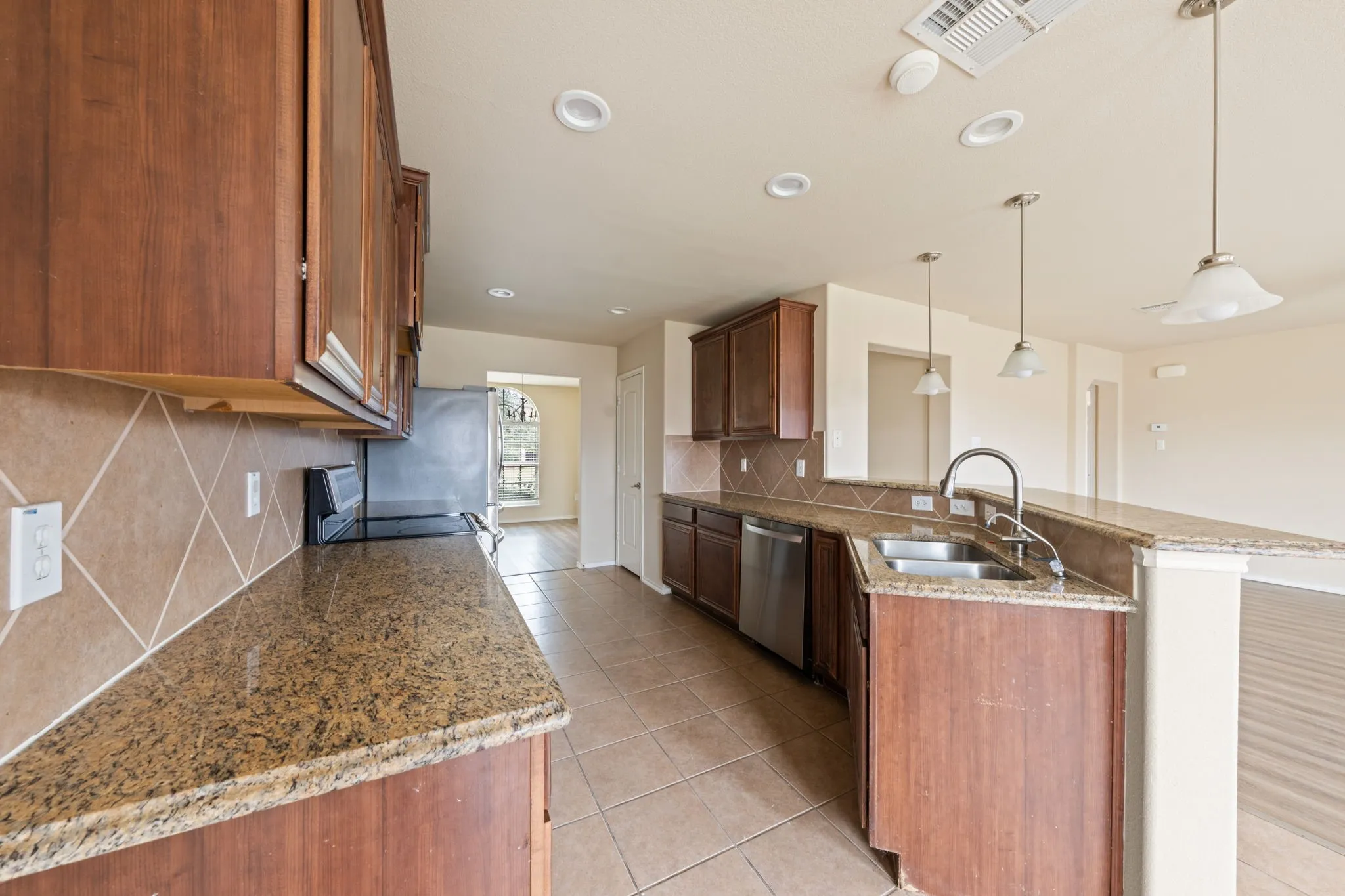 Kitchen featuring a peninsula, dark stone countertops, electric range oven, light tile patterned flooring, and decorative light fixtures