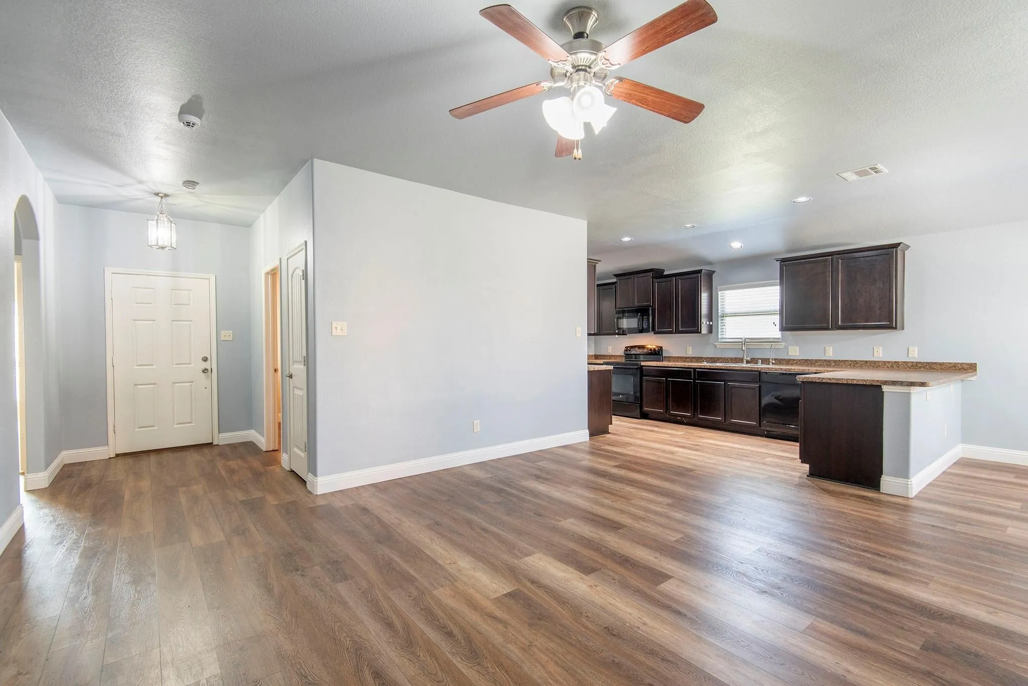 Unfurnished living room with dark wood-style floors, arched walkways, ceiling fan, and recessed lighting