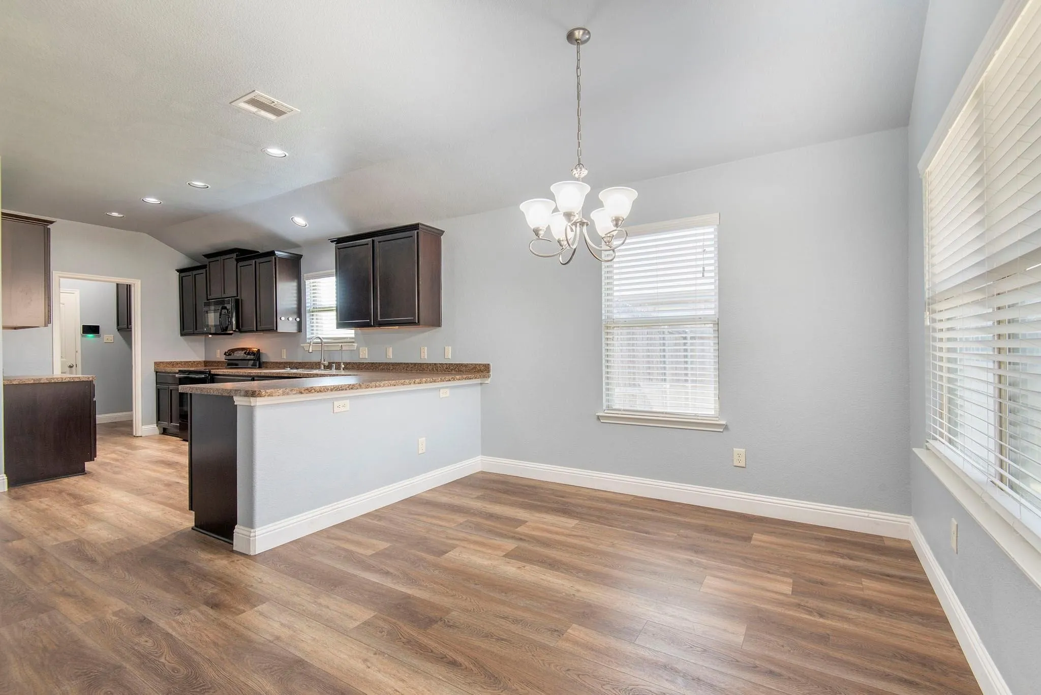 Kitchen with a chandelier, a peninsula, pendant lighting, dark wood finished floors, and lofted ceiling