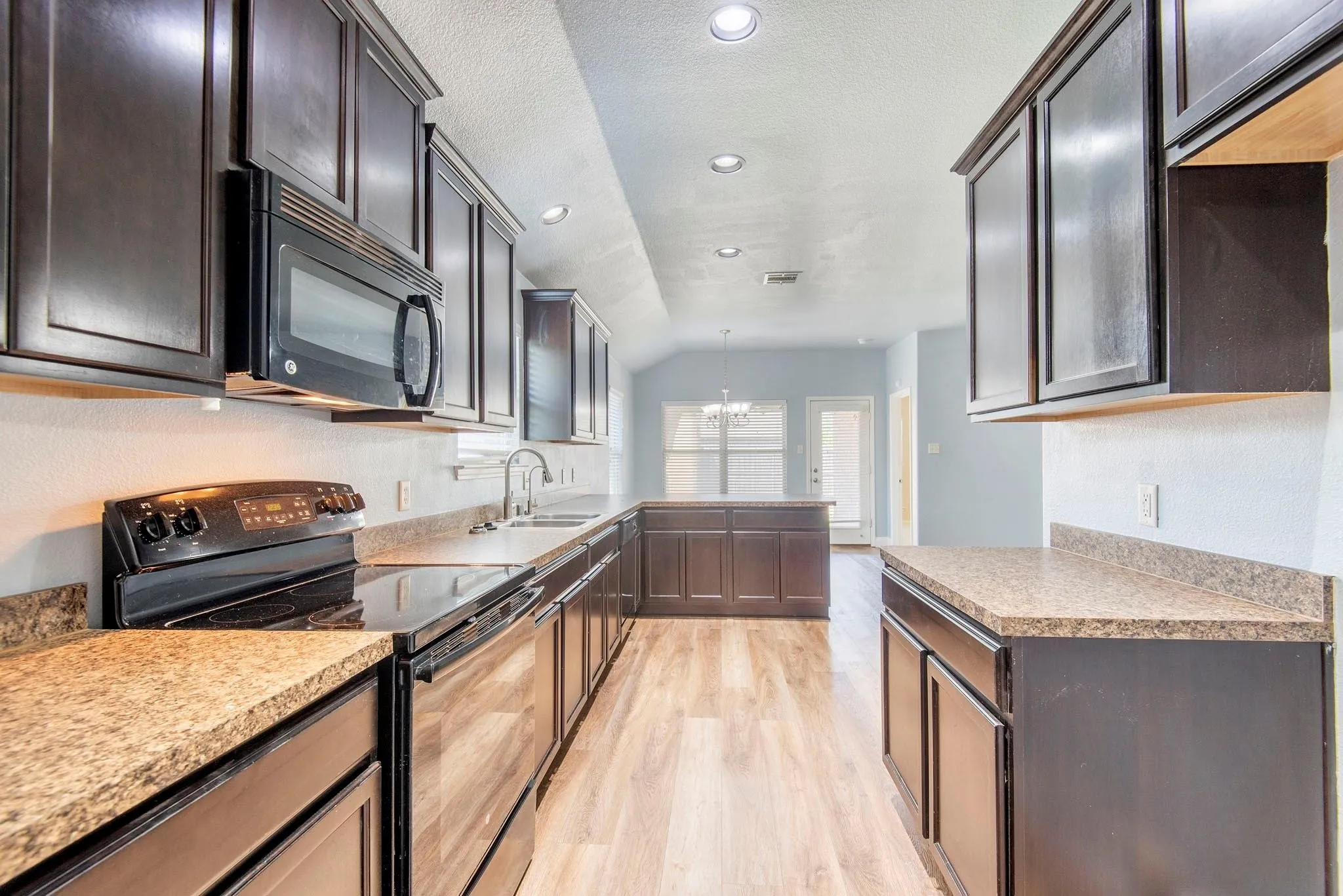 Kitchen with black appliances, a chandelier, dark brown cabinetry, light wood-style floors, and a peninsula