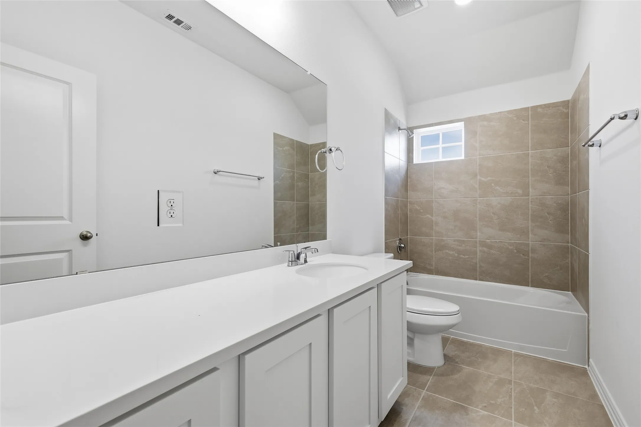 Bathroom featuring a single vanity with a white countertop and undermount sink, a large mirror, a shower-tub combination with tiled surround, and tiled flooring