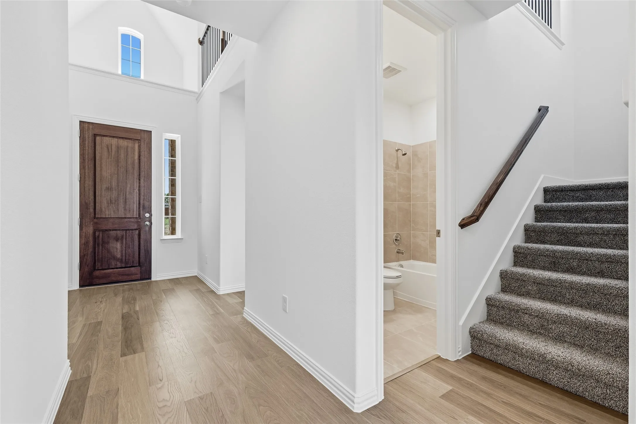 Welcoming foyer showcasing soaring ceilings, a rich wood-finish entry door with sidelights, and wide-plank wood-finish flooring