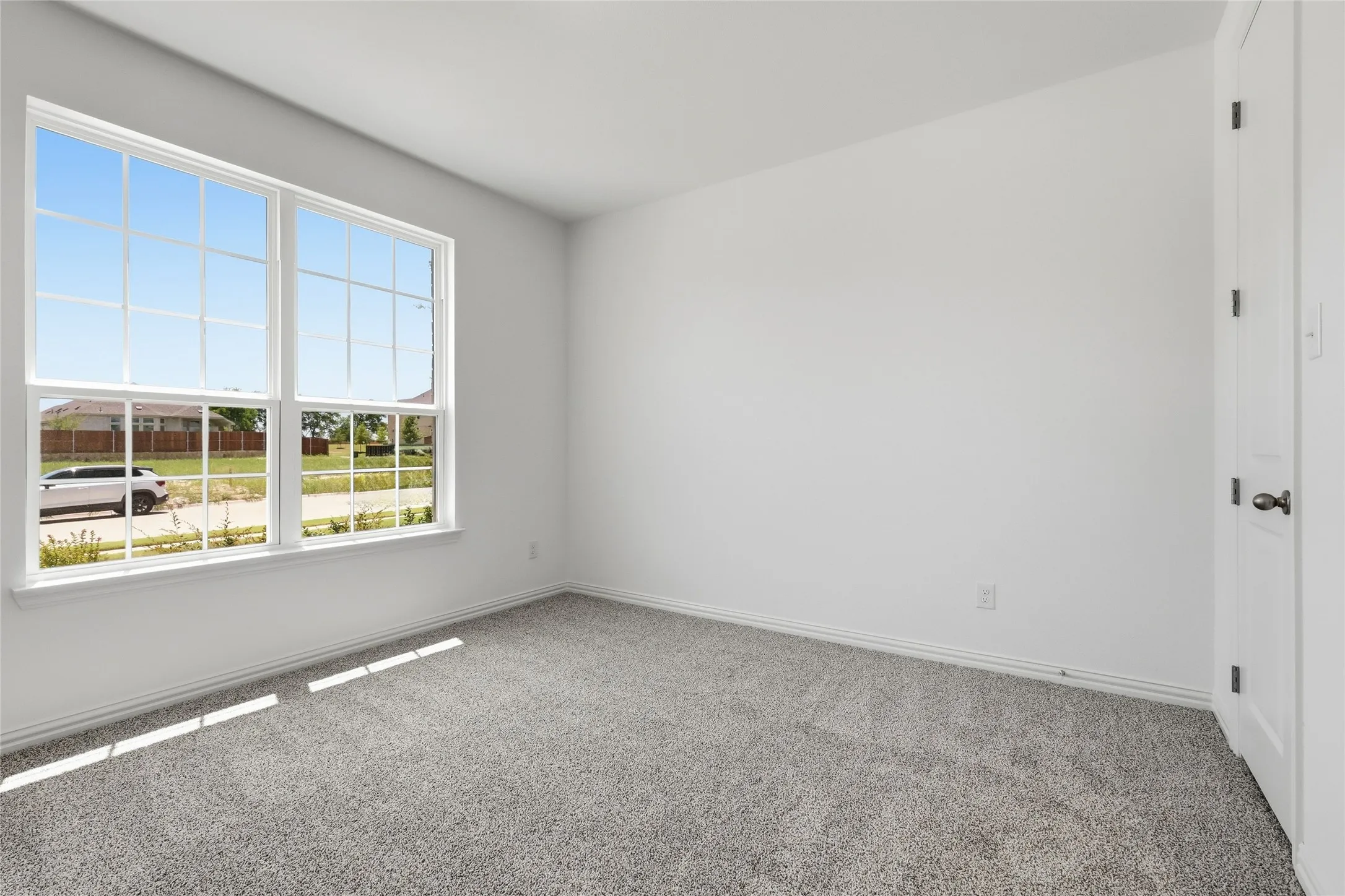 Bright room featuring a large multi-pane window, neutral gray carpet, white baseboards, and a white paneled door with dark hardware