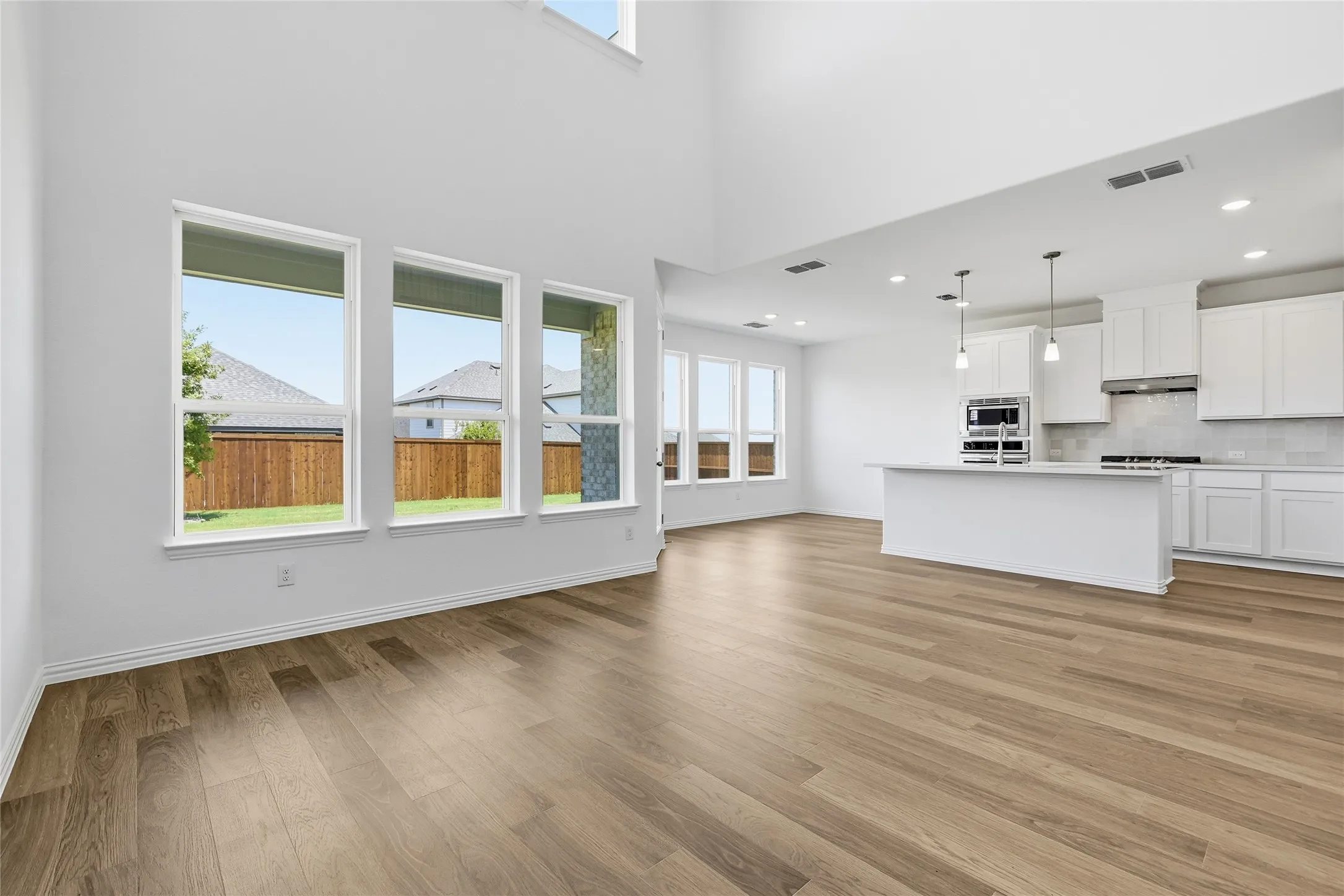 Spacious open-concept living area featuring wood-finish flooring, high ceilings, and abundant natural light from multiple windows