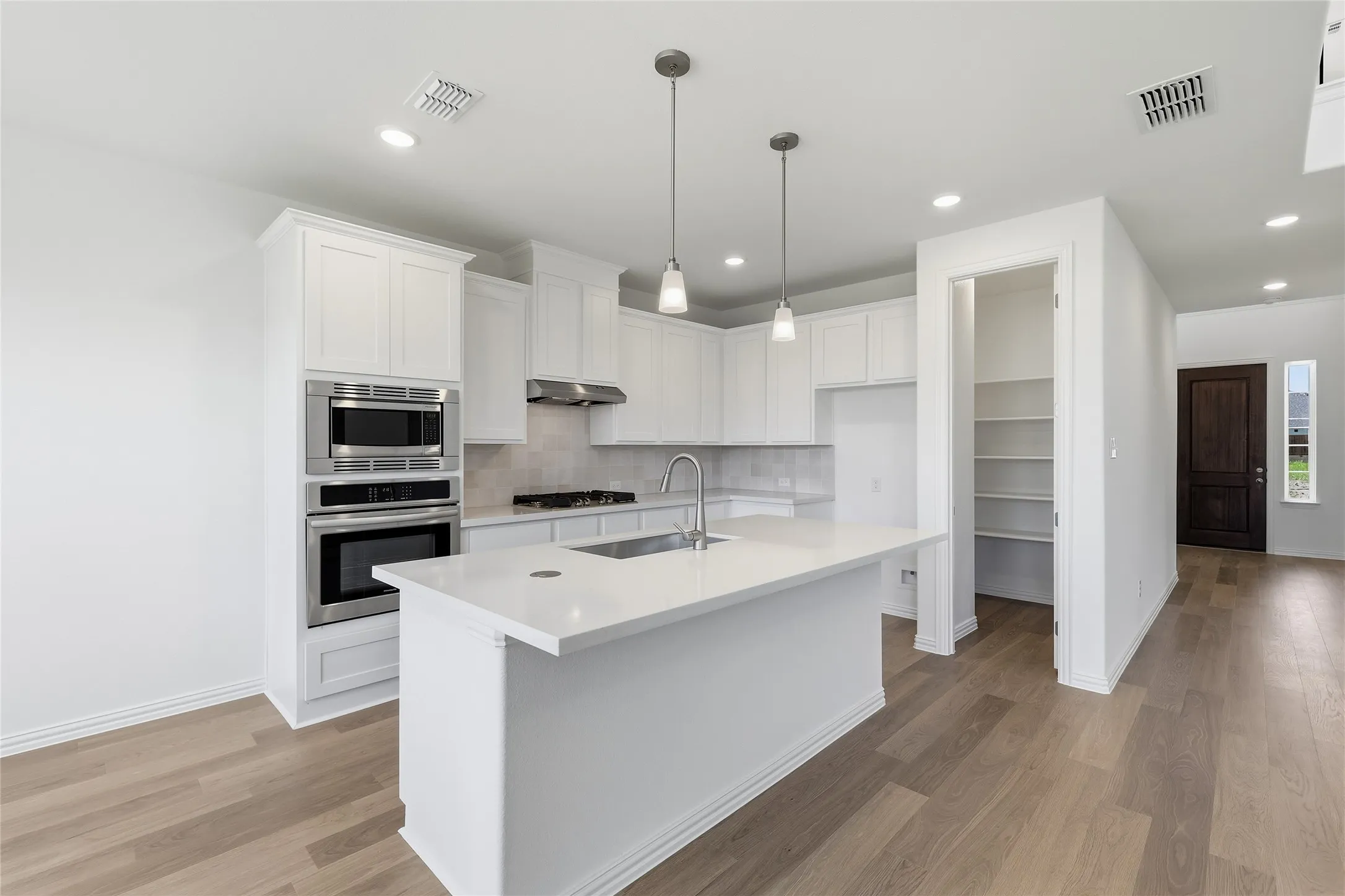 Bright kitchen featuring an island with a sink, white cabinetry, integrated stainless steel appliances, and wood-finish flooring