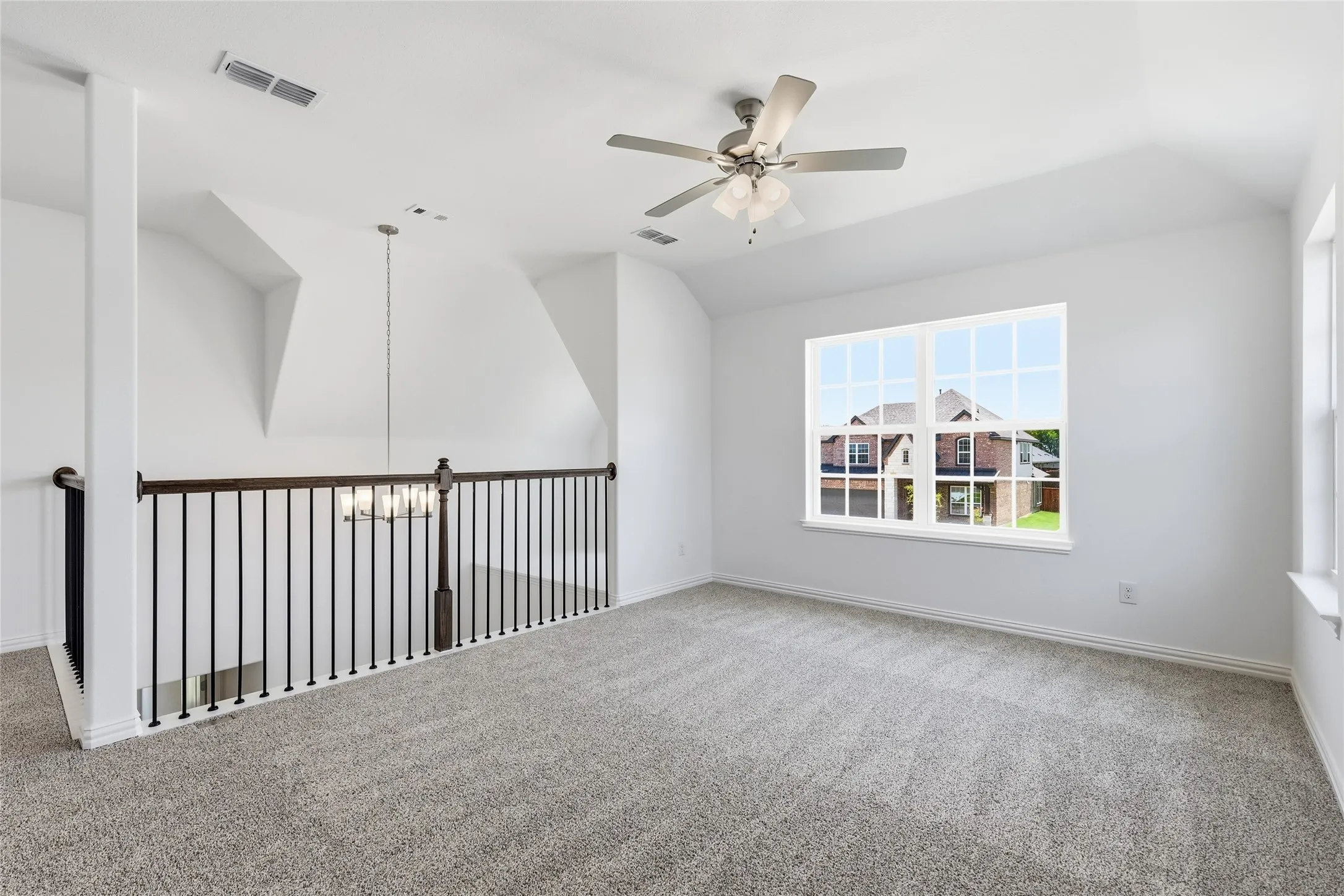 Spacious loft area featuring light gray carpet, a contemporary ceiling fan, and a large multi-pane window