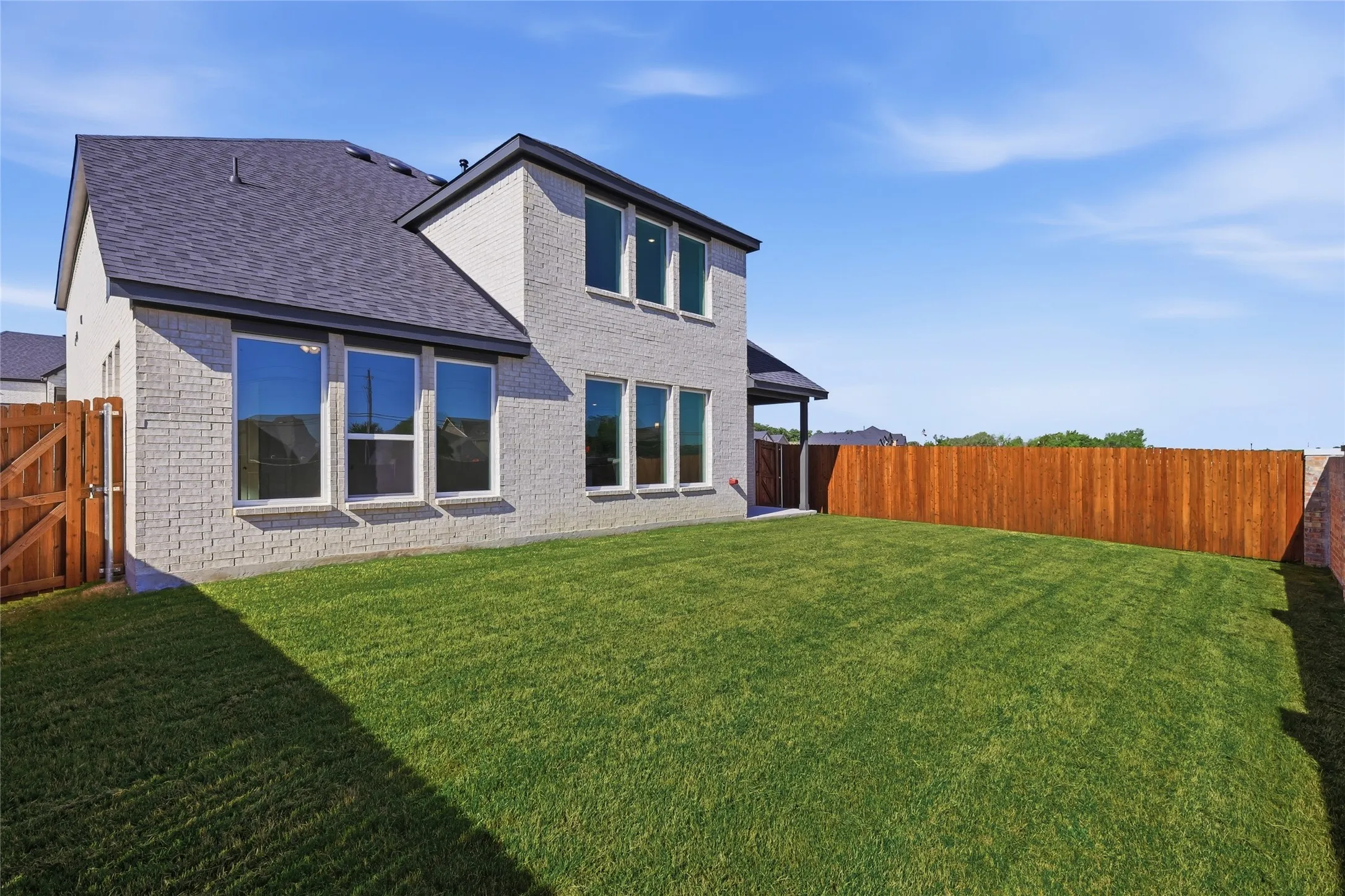 Back of property featuring brick siding, a fenced backyard, roof with shingles, a gate, and a patio