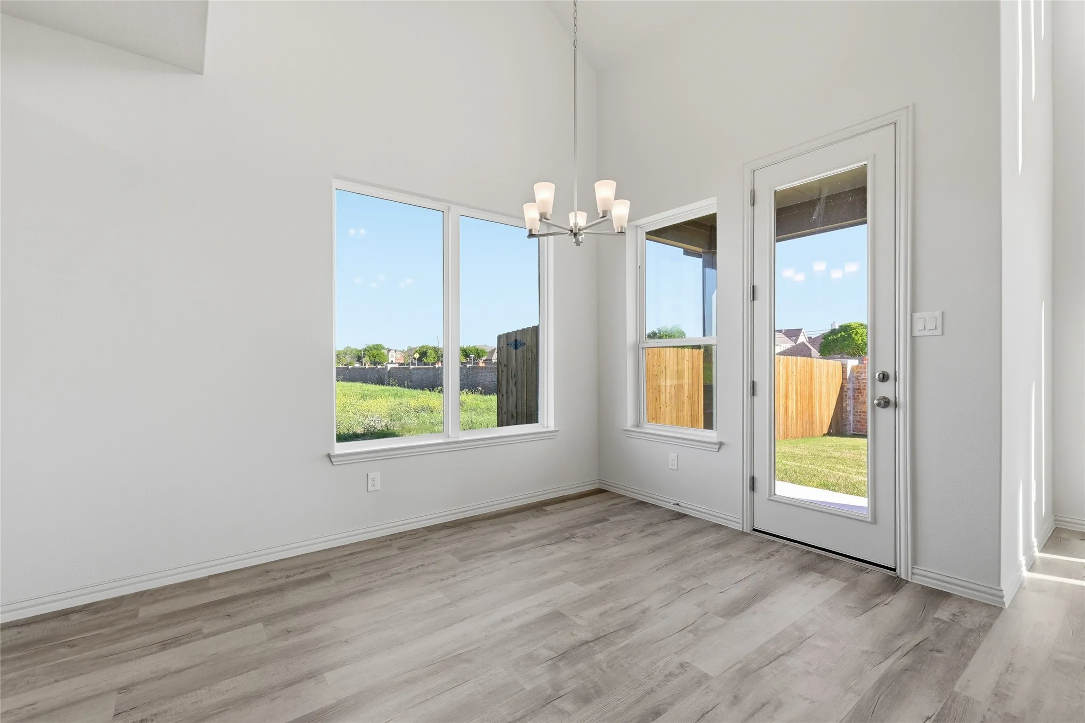 Unfurnished dining area featuring a chandelier, light wood-style flooring, and a high ceiling