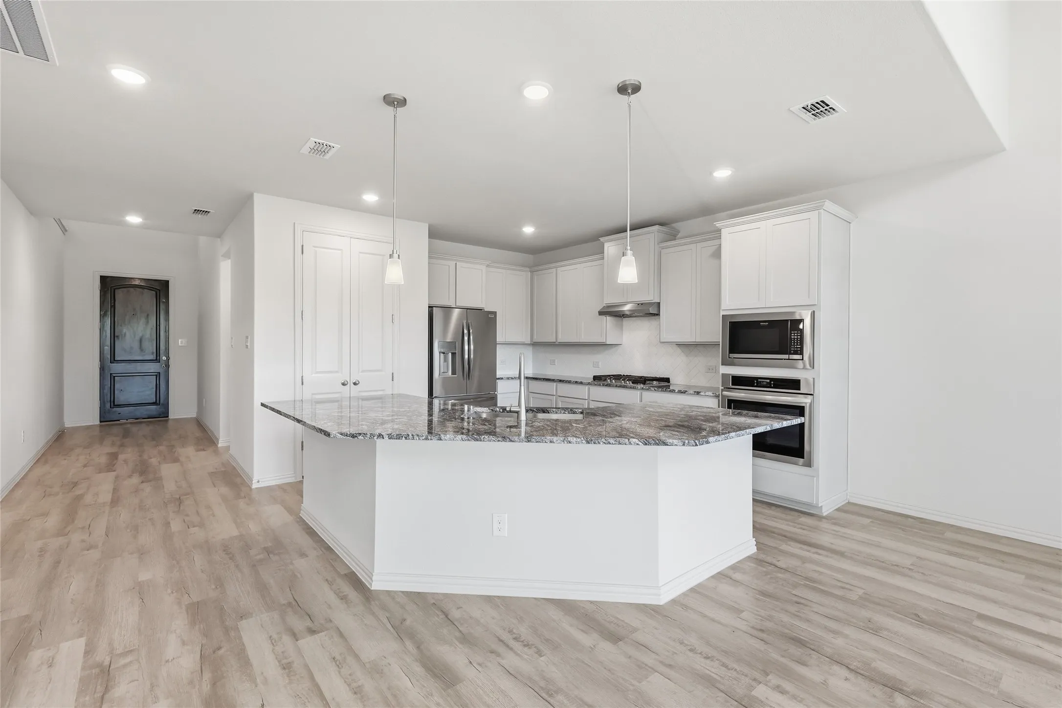 Kitchen with dark stone counters, stainless steel appliances, a kitchen island with sink, white cabinetry, and light wood-style flooring