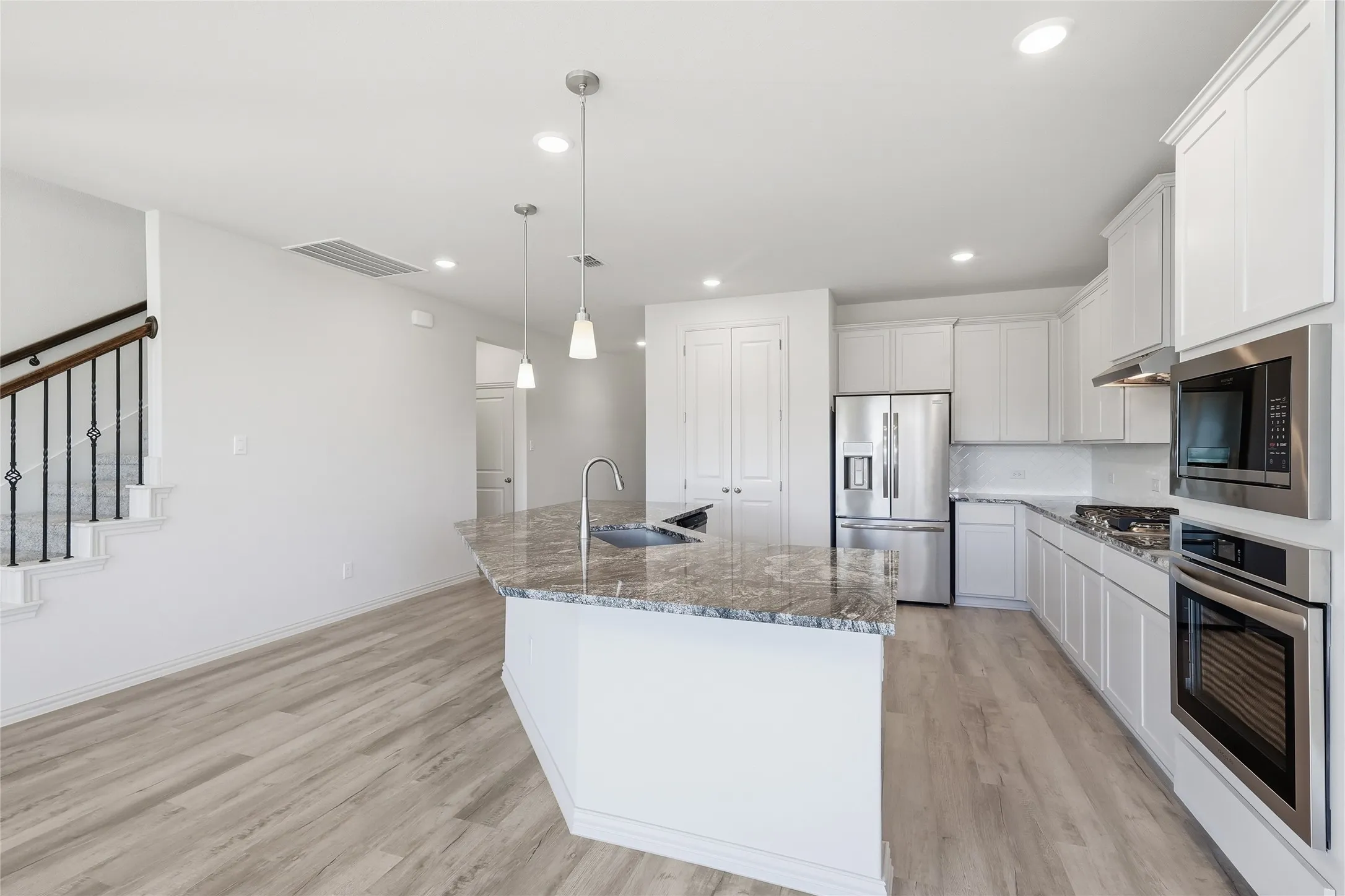 Kitchen featuring stainless steel appliances, a large island, white cabinetry, light wood-style flooring, and light stone countertops