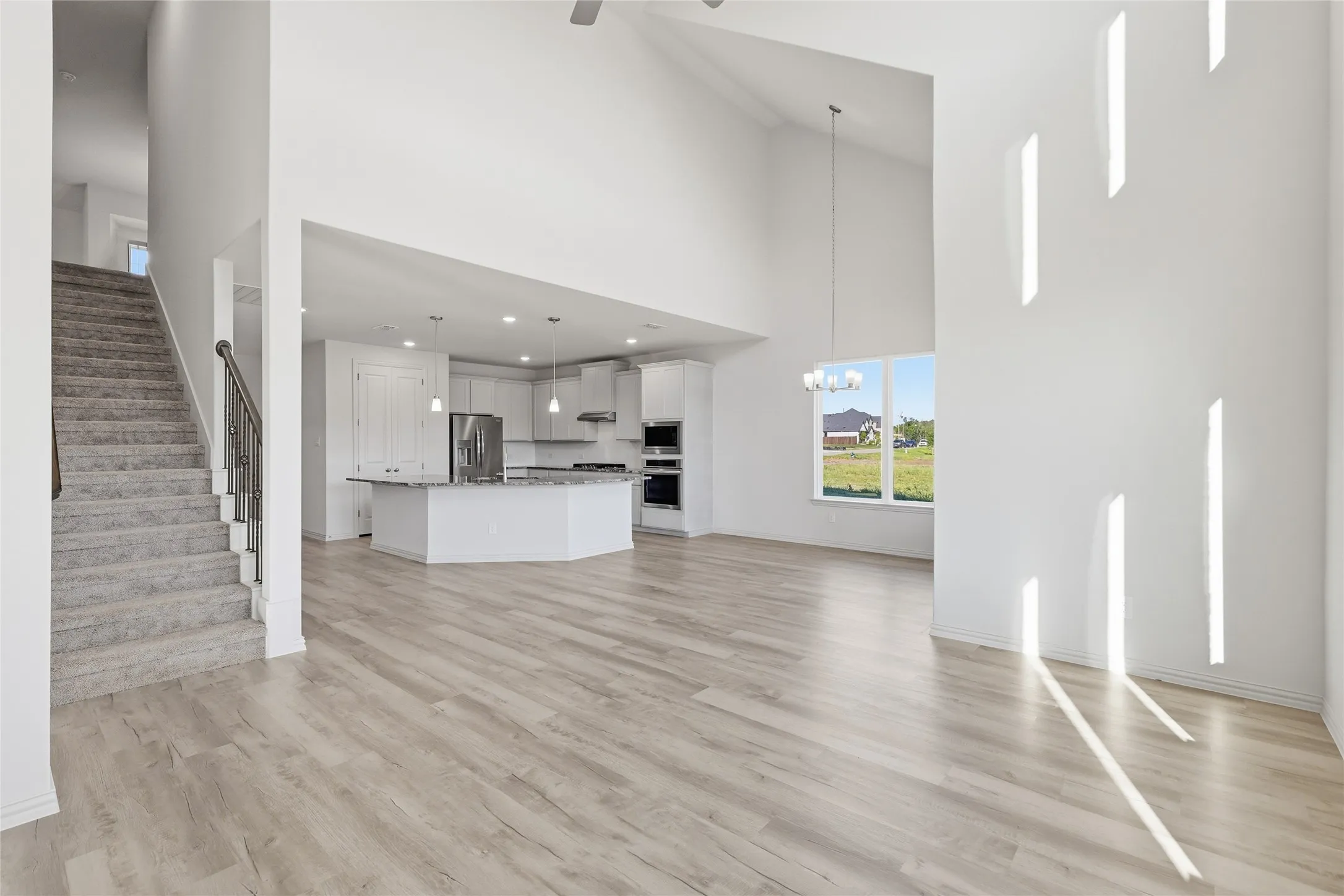 Unfurnished living room featuring light wood finished floors, a high ceiling, suspended lighting, and ceiling fan