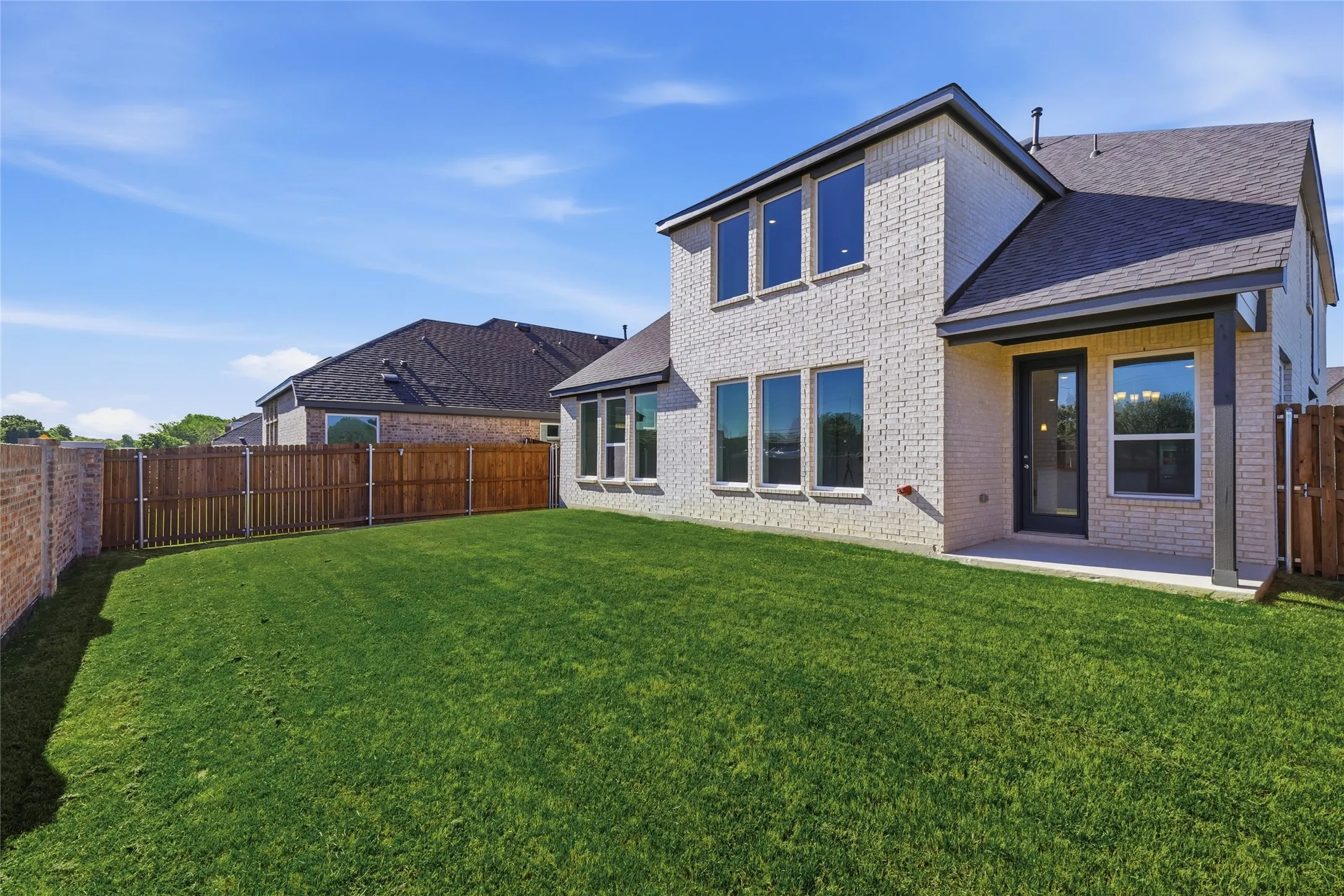 Back of property with brick siding, a patio, a fenced backyard, and roof with shingles