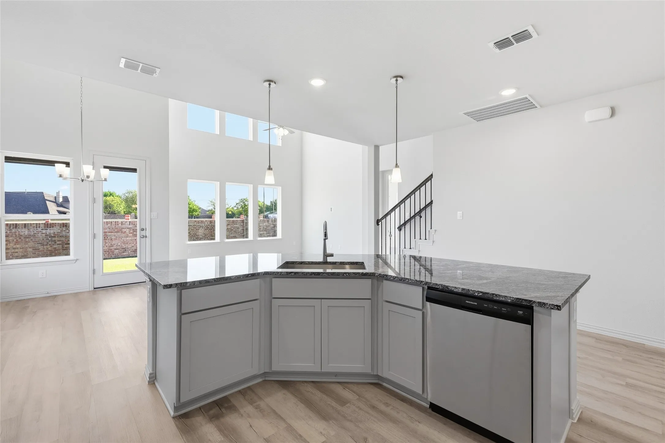 Kitchen with an island with sink, dishwasher, gray cabinetry, light wood-style floors, and pendant lighting