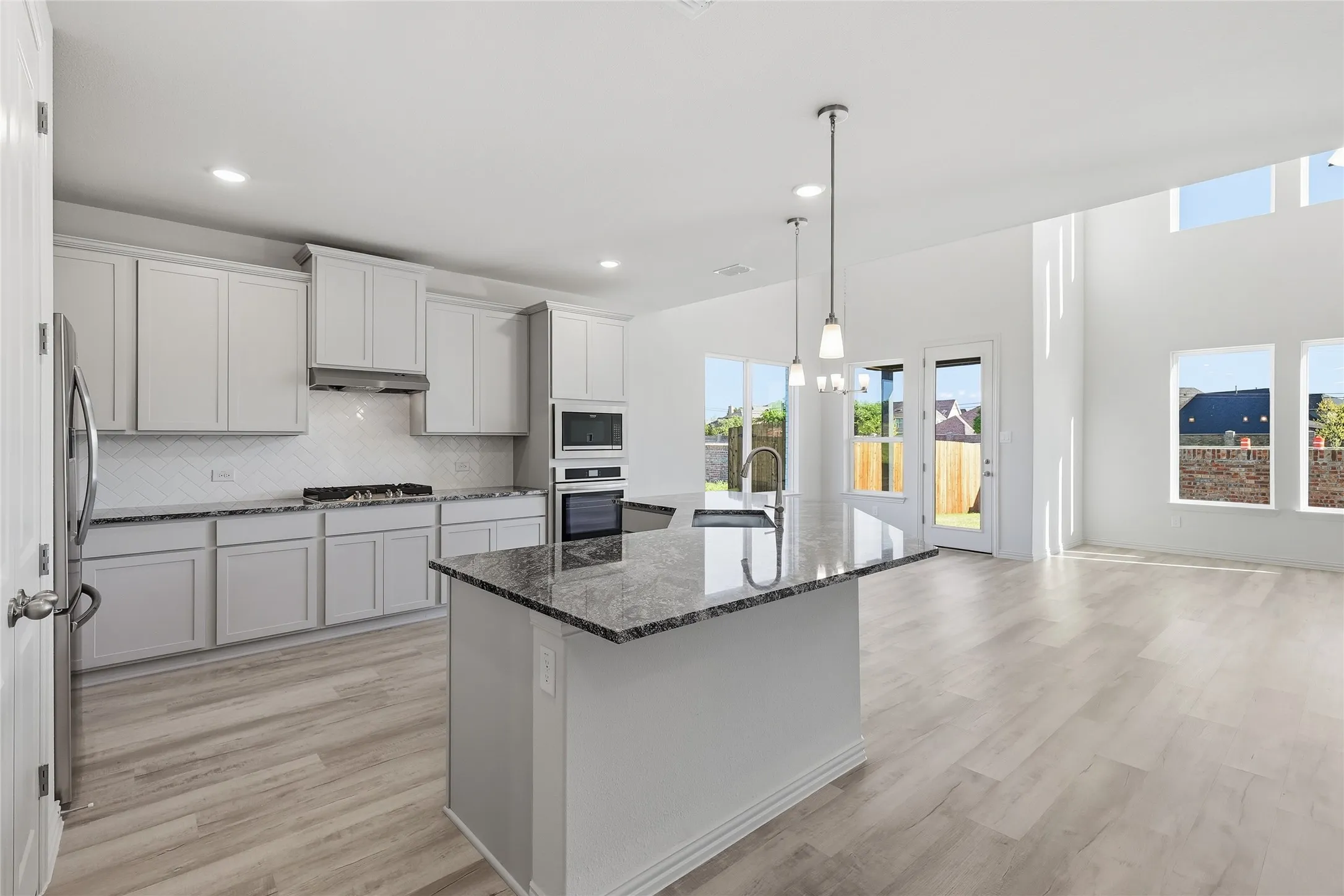 Kitchen with dark stone countertops, decorative backsplash, light wood-type flooring, an island with sink, and decorative light fixtures