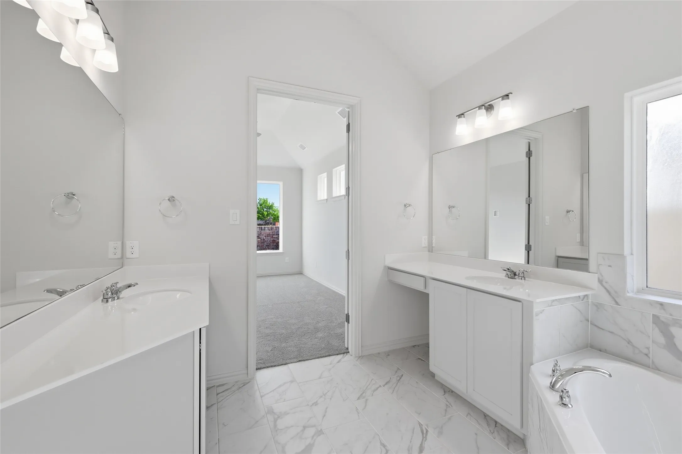 Full bathroom with light marble finish floors, two vanities, a garden tub, and lofted ceiling