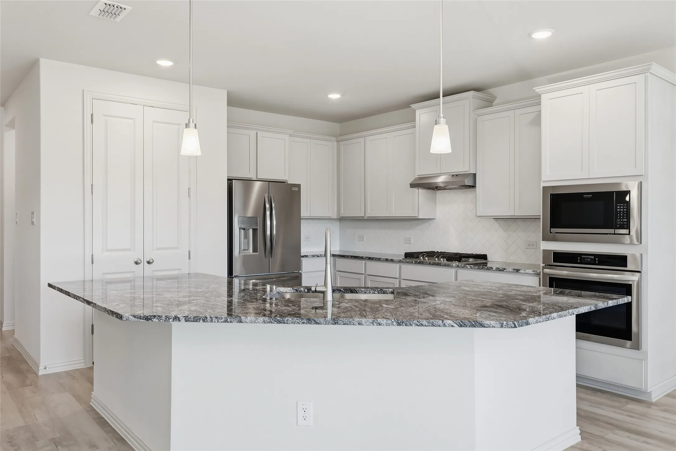 Kitchen featuring light wood-style floors, stainless steel appliances, a kitchen island with sink, and backsplash
