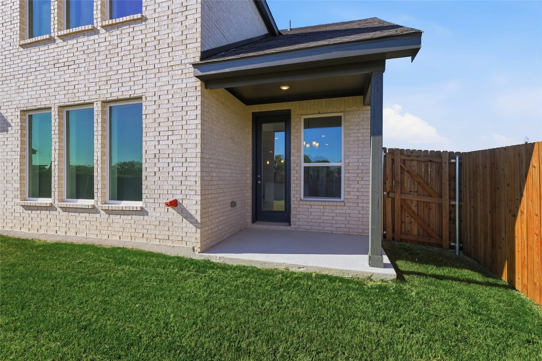 Property entrance with a patio area, brick siding, a yard, and a gate