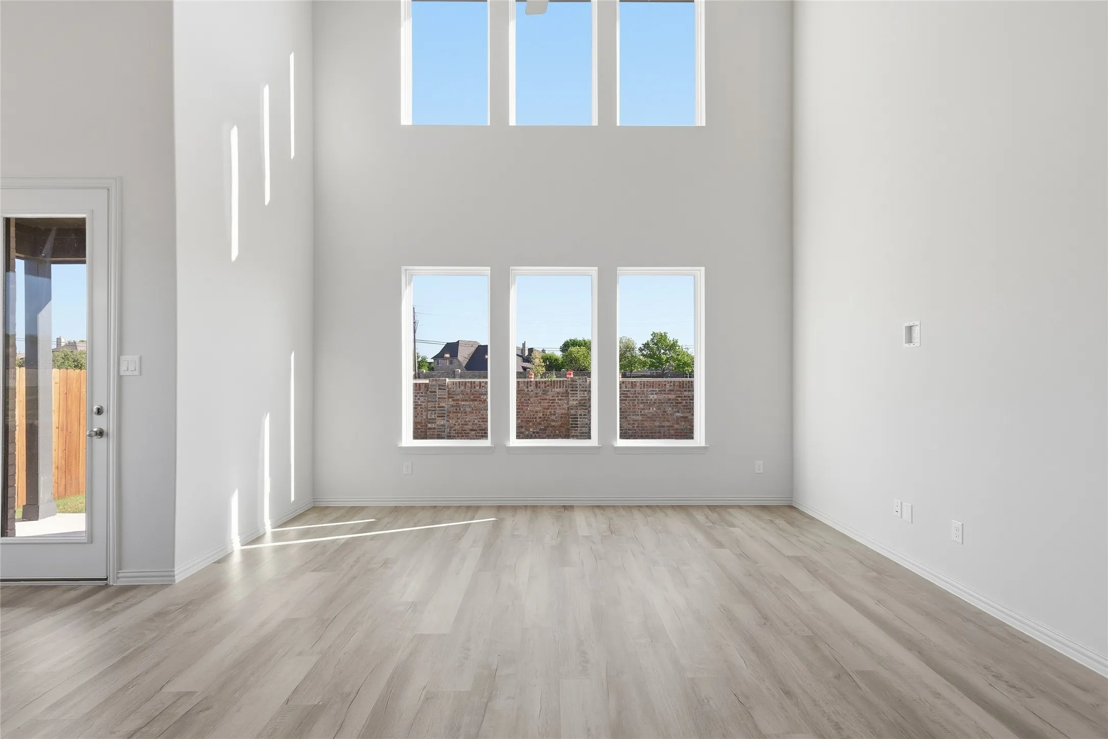 Unfurnished living room featuring healthy amount of natural light, light wood-style floors, and a high ceiling