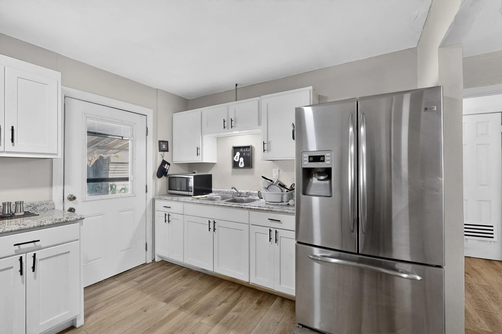 Kitchen featuring stainless steel appliances, white cabinetry, light wood-type flooring, and light stone counters