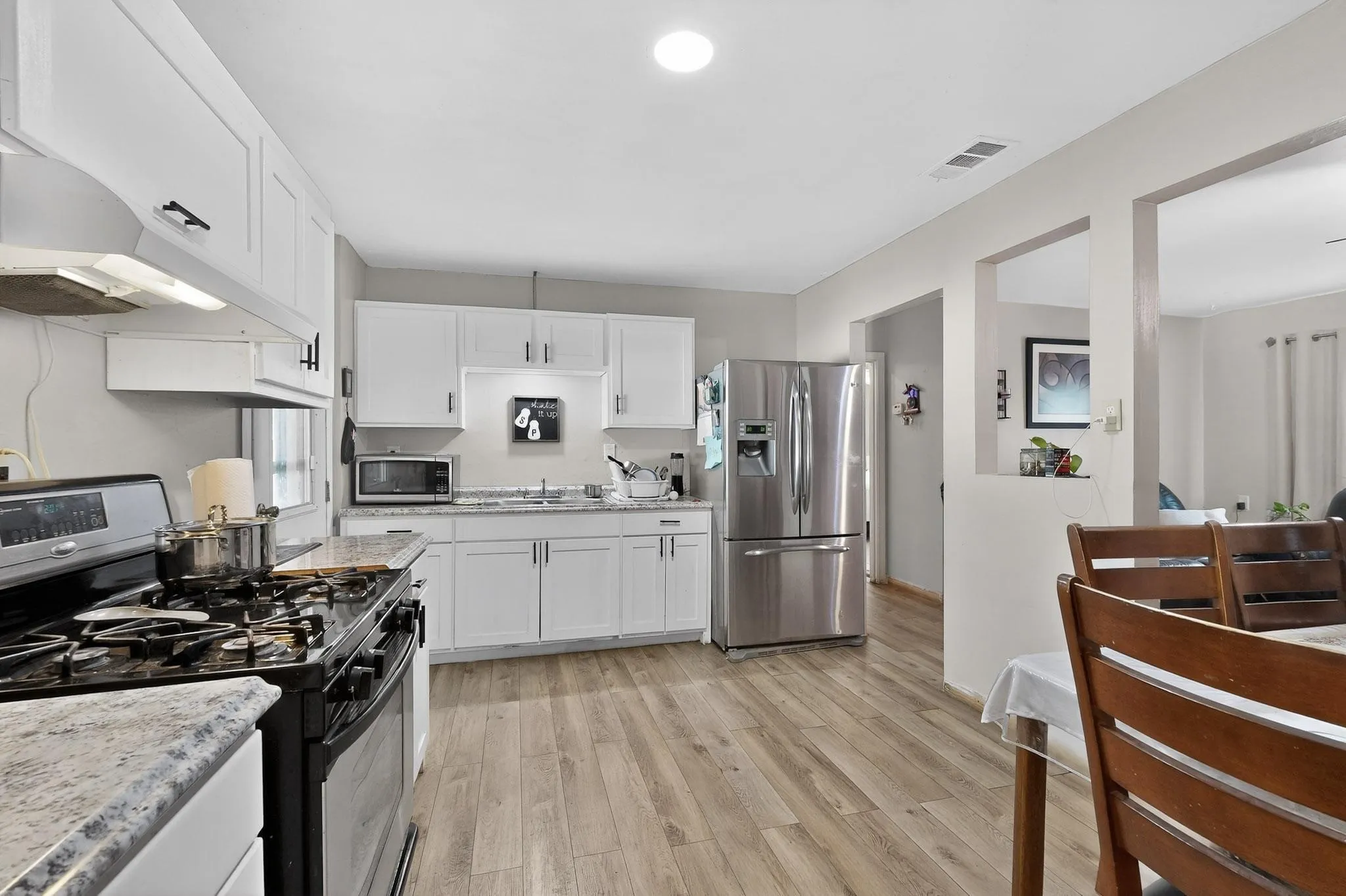 Kitchen featuring stainless steel appliances, white cabinets, light wood-type flooring, and light stone countertops