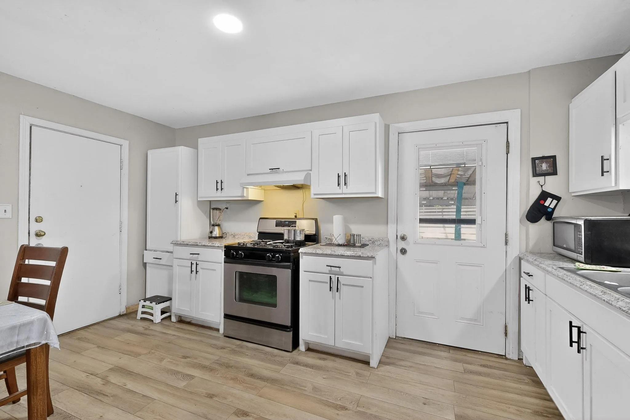 Kitchen featuring stainless steel appliances, white cabinets, light wood-type flooring, and light stone counters