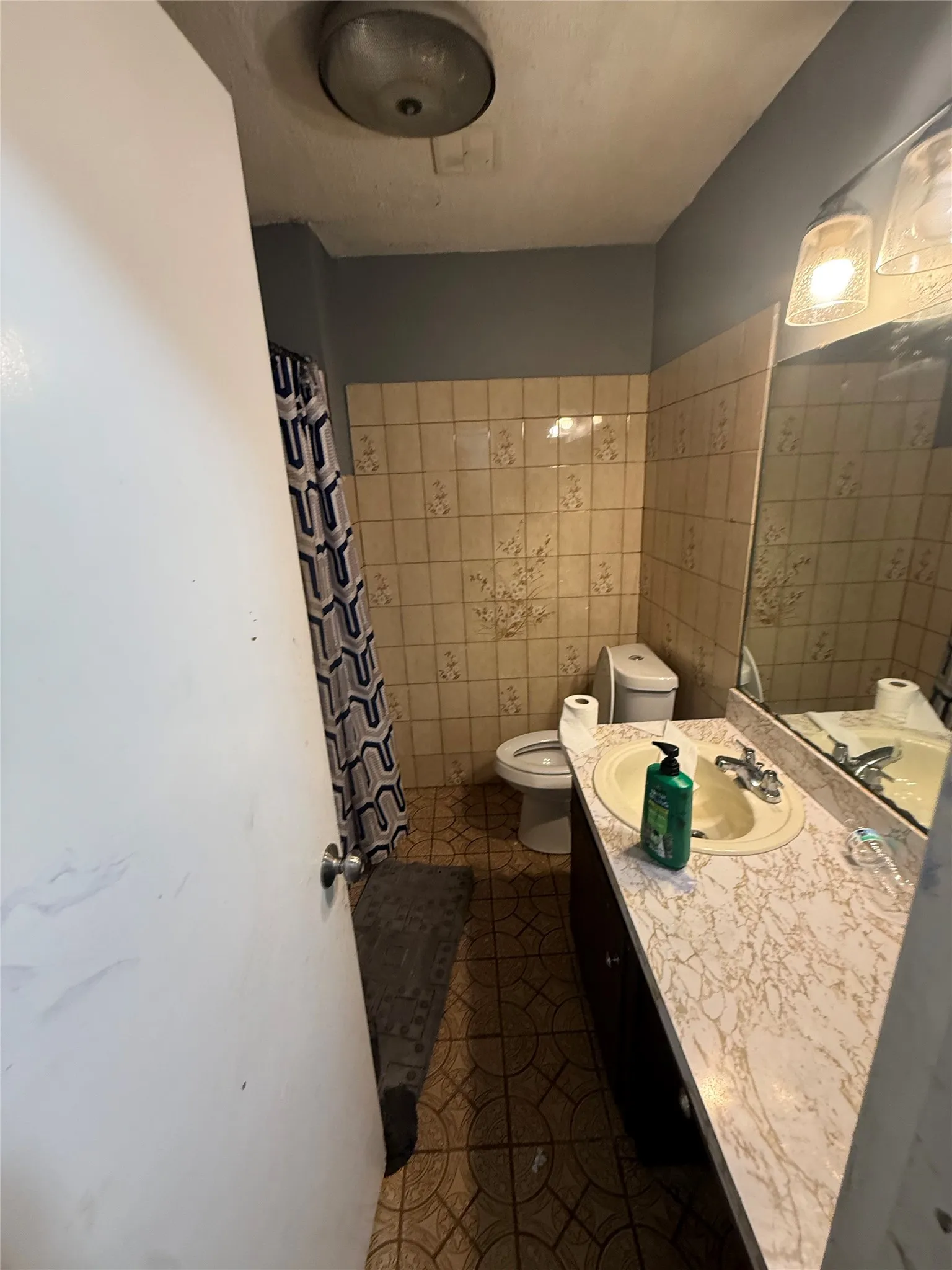 Full bath featuring vanity, a shower with shower curtain, tile walls, and dark tile patterned floors