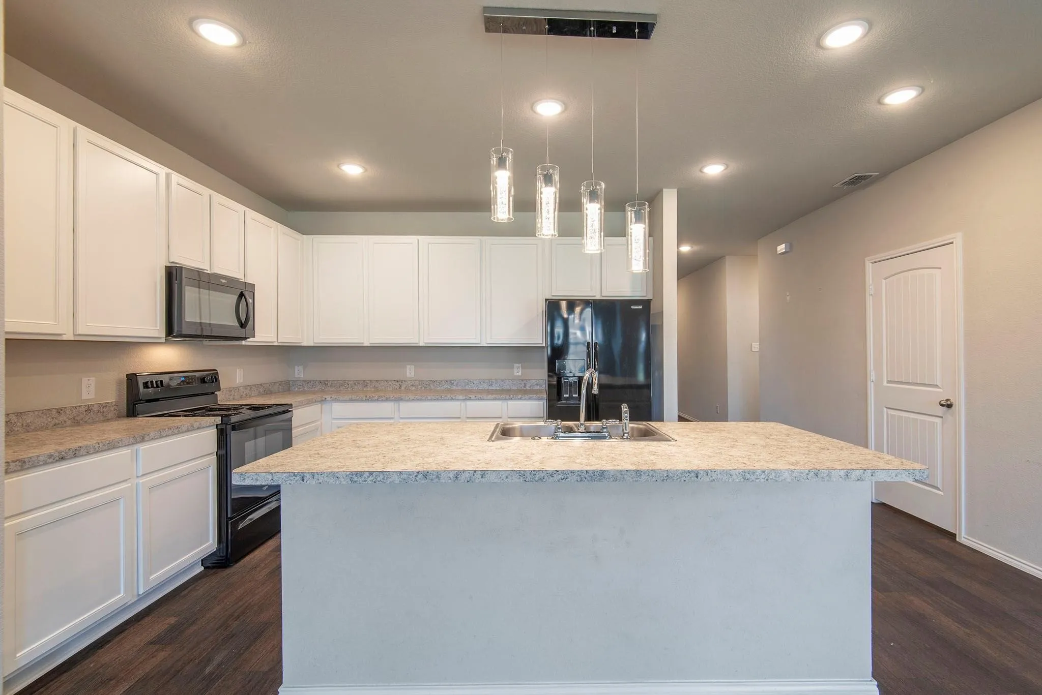 Kitchen featuring an island with an undermount sink, white cabinetry, black appliances, recessed lighting, and wood-finish flooring