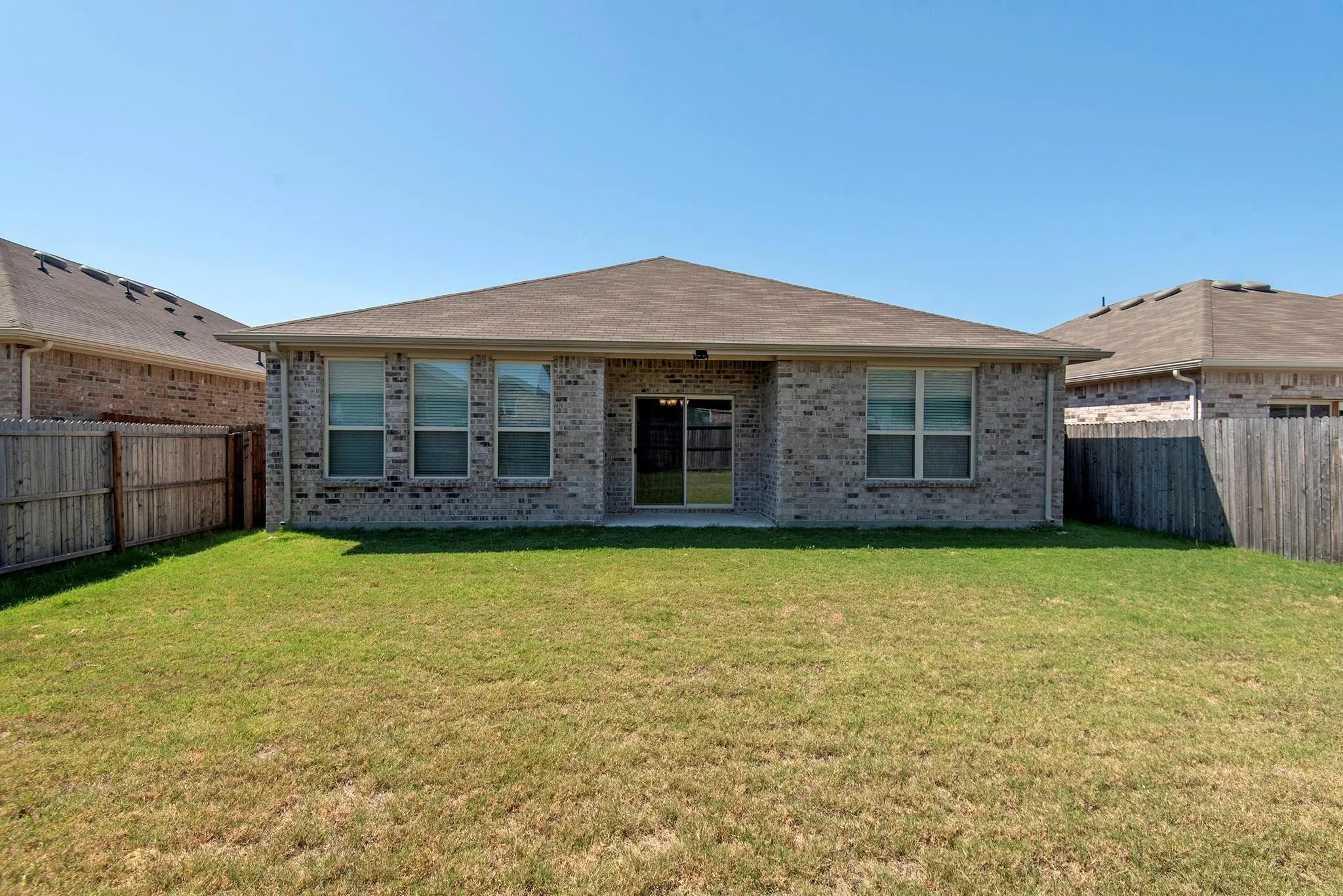 Rear view of house featuring brick siding, a fenced backyard, and a patio area