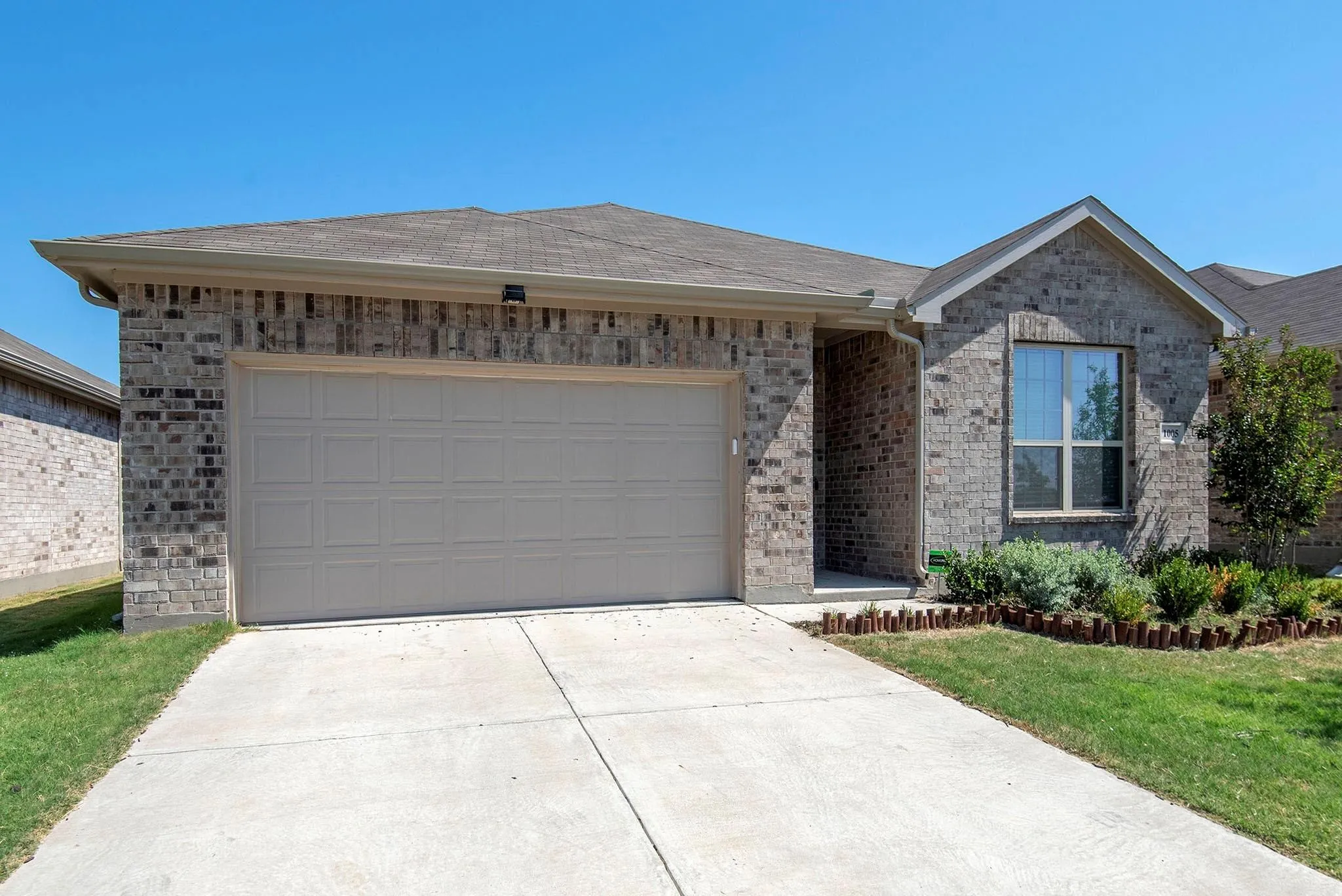 Brick exterior with an attached garage, concrete driveway, and front landscaping