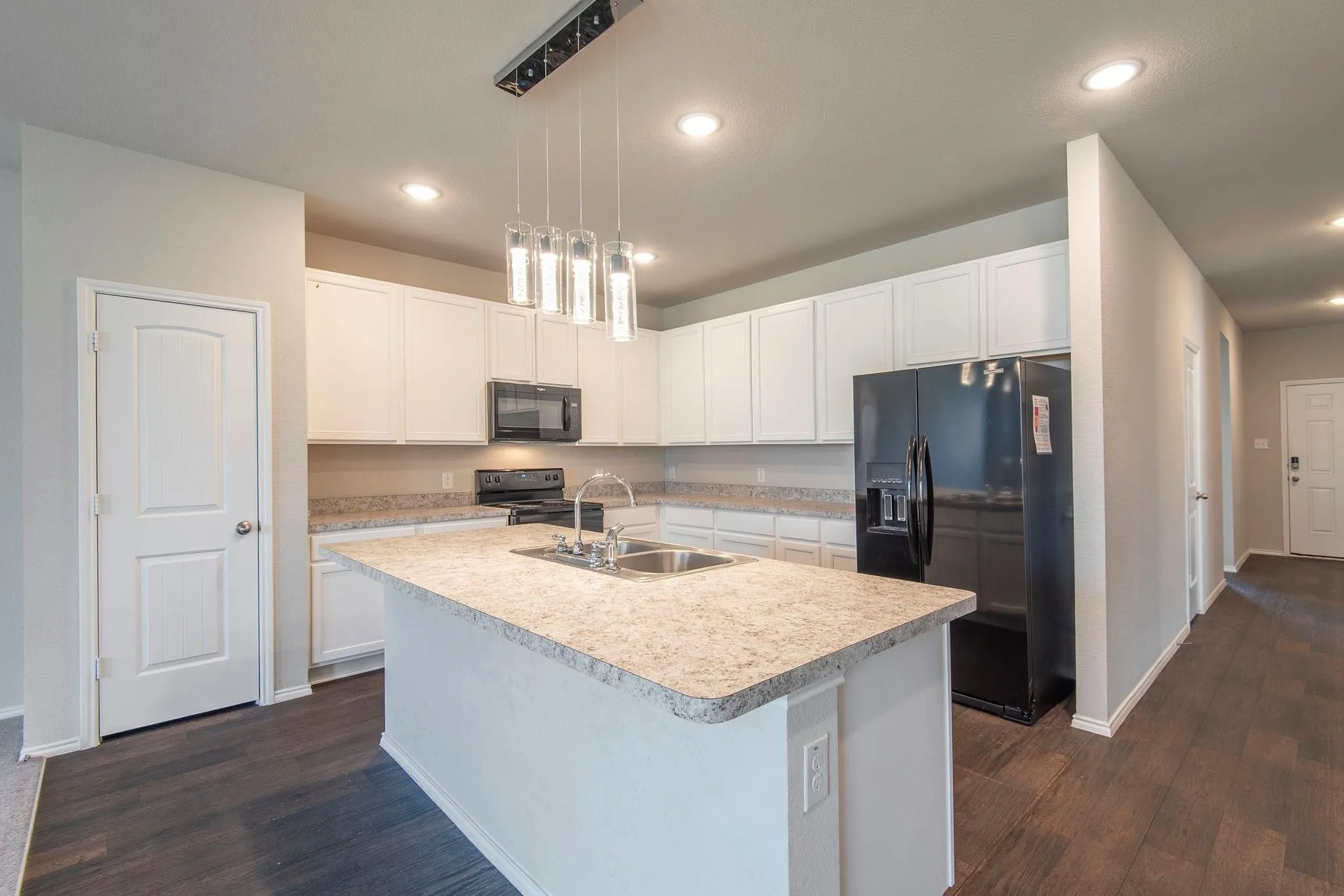 Modern kitchen featuring white cabinetry, quartz countertops, a large waterfall-edge island with seating, stainless steel appliances including a black refrigerator, pendant lighting, and wood-finish flooring throughout