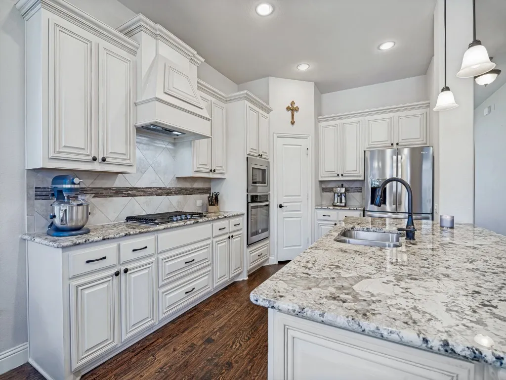 Kitchen featuring white cabinets, stainless steel appliances, light stone counters, and dark wood finished floors