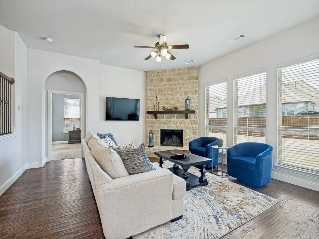 Living room with a fireplace, a ceiling fan, dark wood-type flooring, and arched walkways