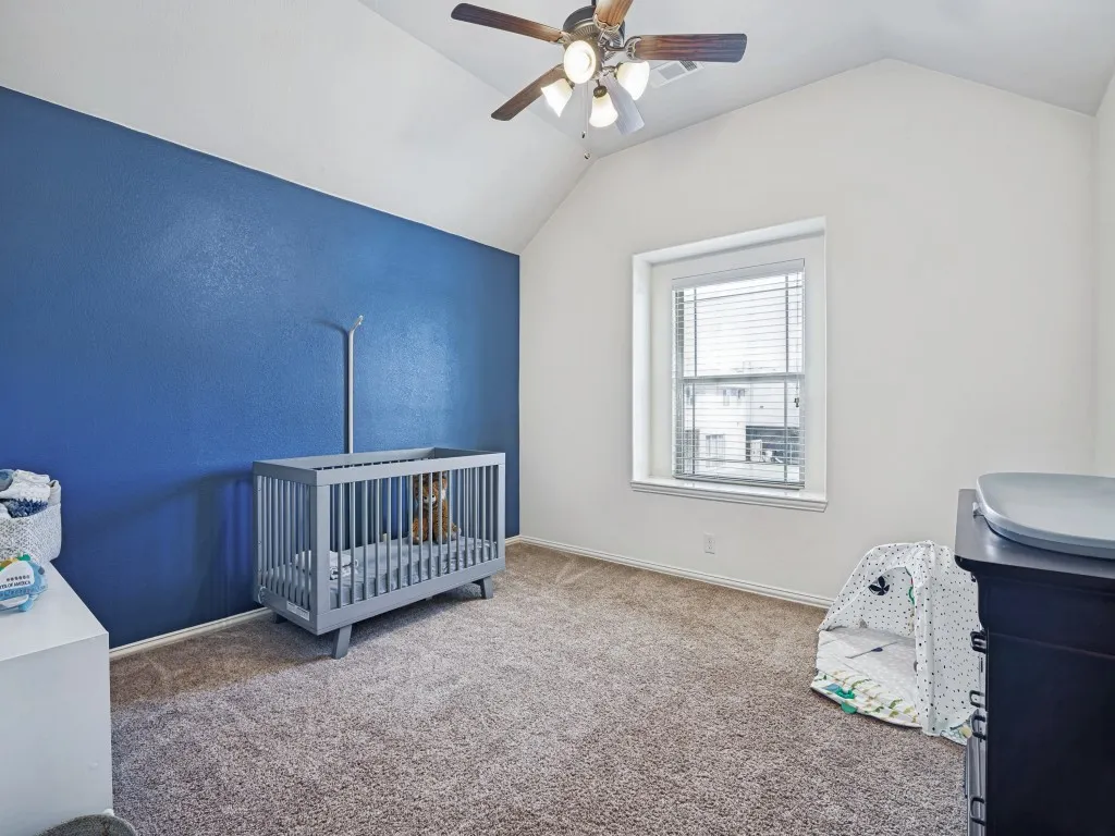 Carpeted bedroom with a crib and ceiling fan
