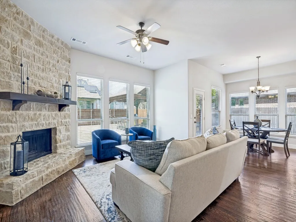 Living room featuring dark wood-style flooring, a stone fireplace, a chandelier, and healthy amount of natural light
