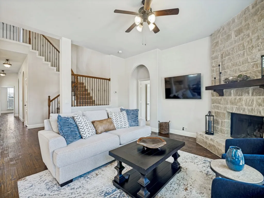 Living room featuring dark wood-style flooring, ceiling fan, a fireplace, and arched walkways