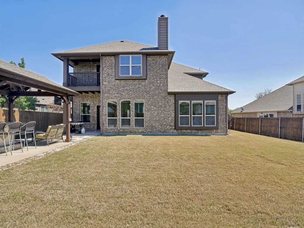 Back of house featuring a fenced backyard, a balcony, brick siding, a patio, and a chimney