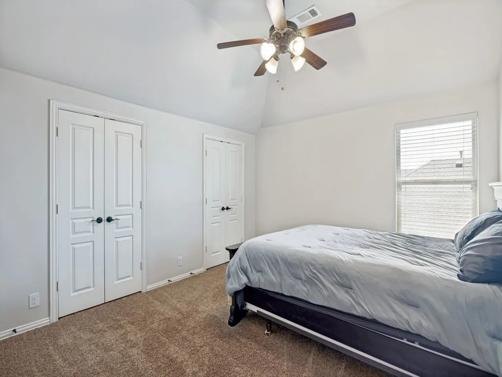 Bedroom featuring two closets, dark colored carpet, lofted ceiling, and ceiling fan