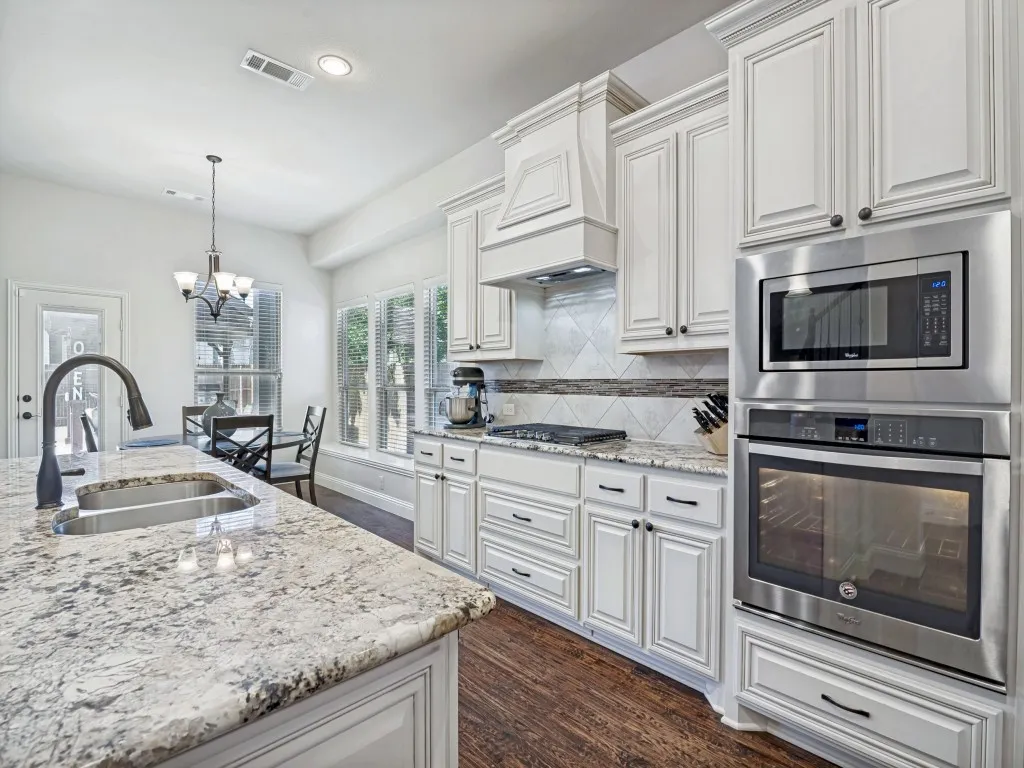 Kitchen featuring stainless steel appliances, light stone countertops, a chandelier, and white cabinets