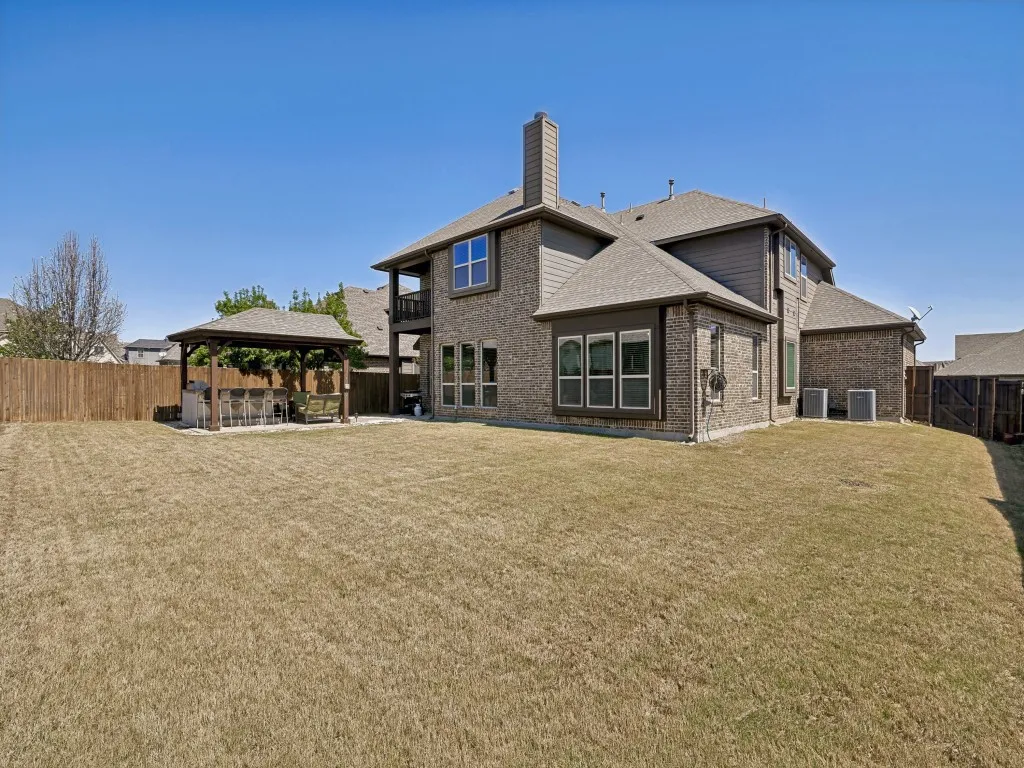 Rear view of house with a fenced backyard, brick siding, a patio, a gazebo, and a chimney