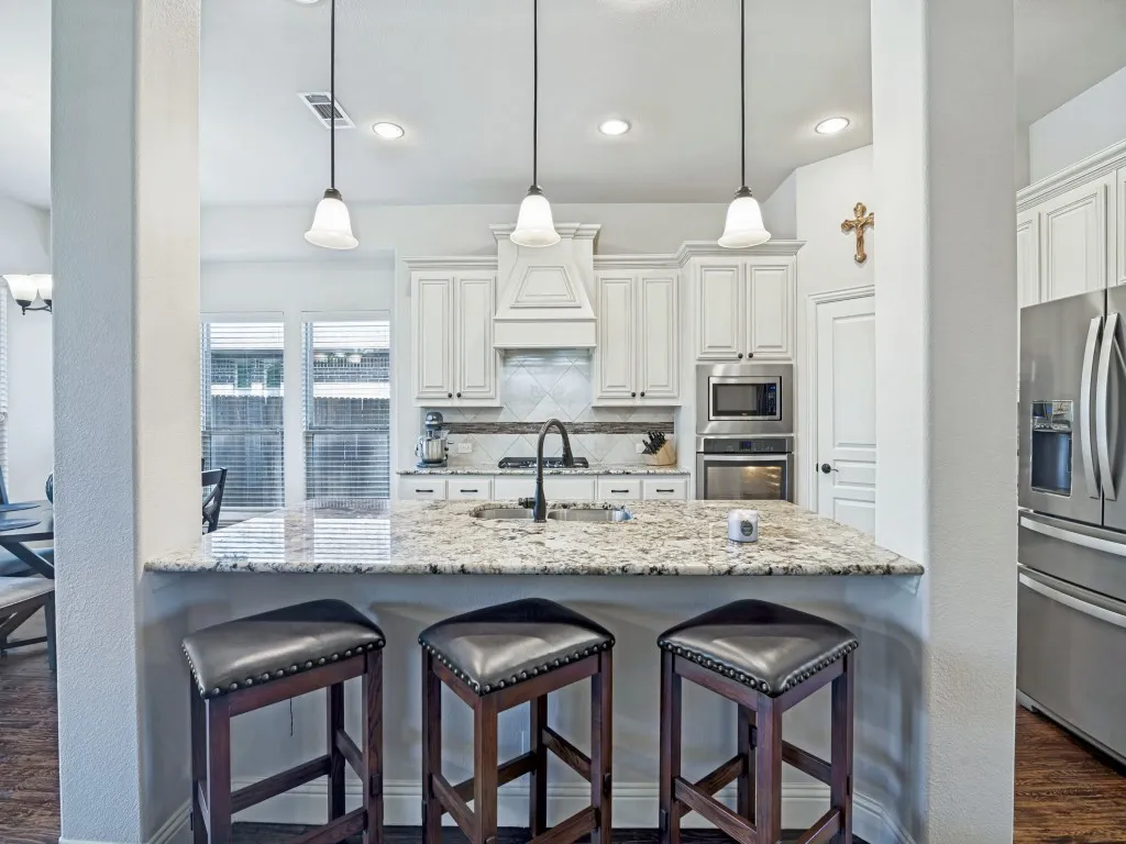 Kitchen with stainless steel appliances, decorative backsplash, decorative light fixtures, a breakfast bar, and light stone counters
