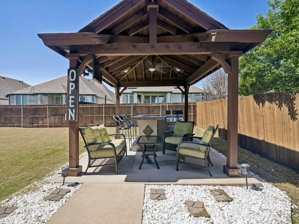 Fenced backyard with a patio, a gazebo, an outdoor kitchen and area to lounge, and a ceiling fan