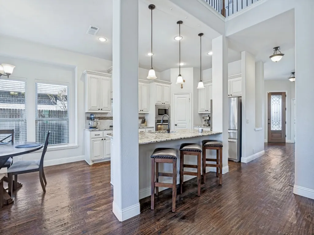 Kitchen featuring dark wood-style flooring, decorative light fixtures, white cabinetry, light stone counters, and a kitchen bar