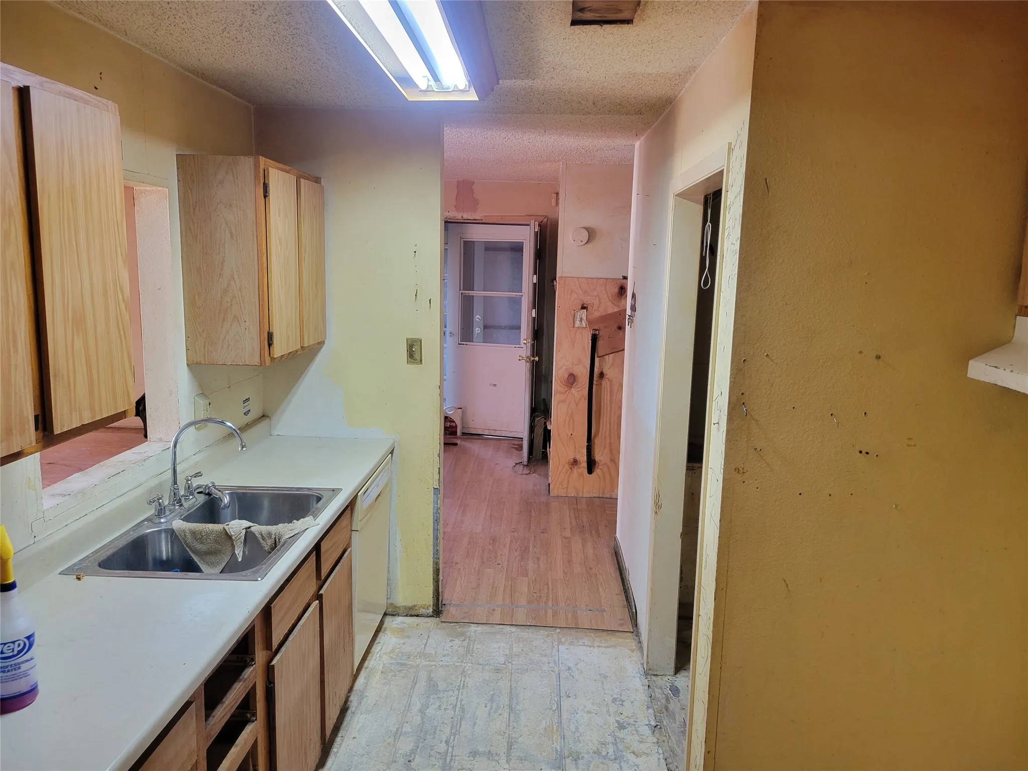 Kitchen with light countertops, a textured ceiling, dishwasher, light wood finish cabinetry, and light wood-style flooring